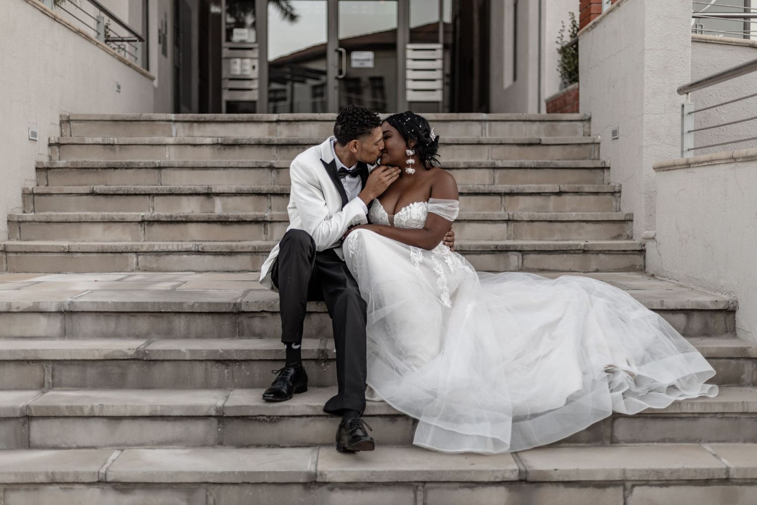 Romantic wedding couple sitting together on white stone steps.
