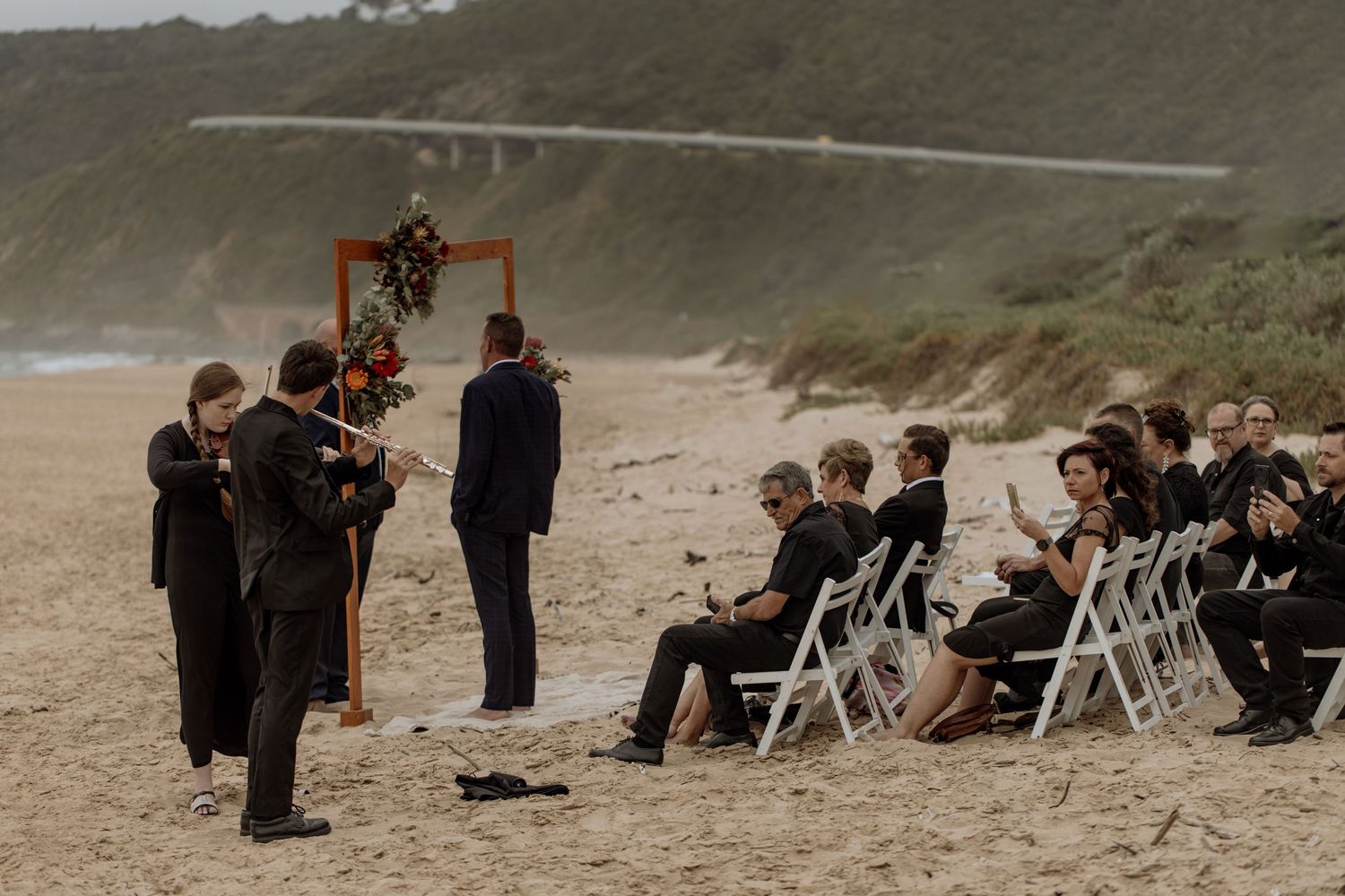 A small beach wedding ceremony setup with folding chairs and wedding party gathered on a misty coastline.