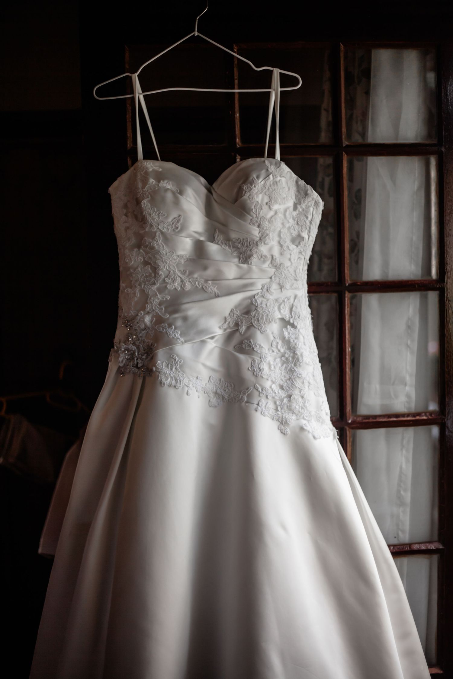 A white wedding dress with delicate lace bodice hangs on a wooden hanger against a dark background in multiple views.