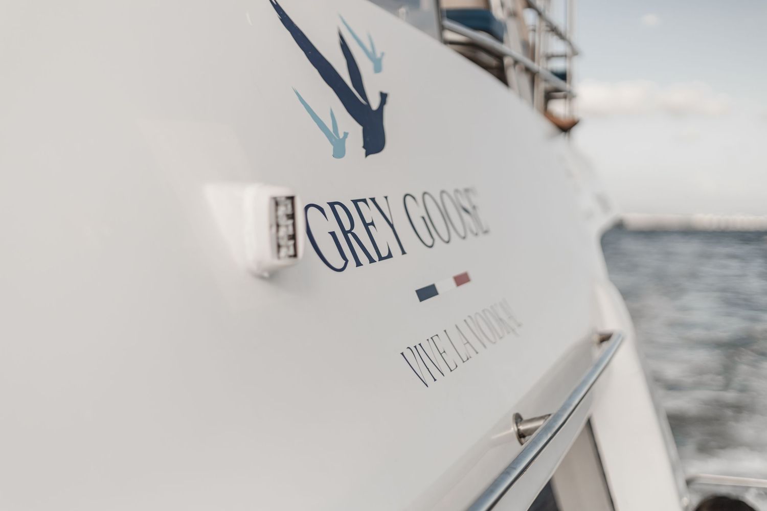 Close-up view of Grey Goose branding on a white boat hull against a blurry water background.