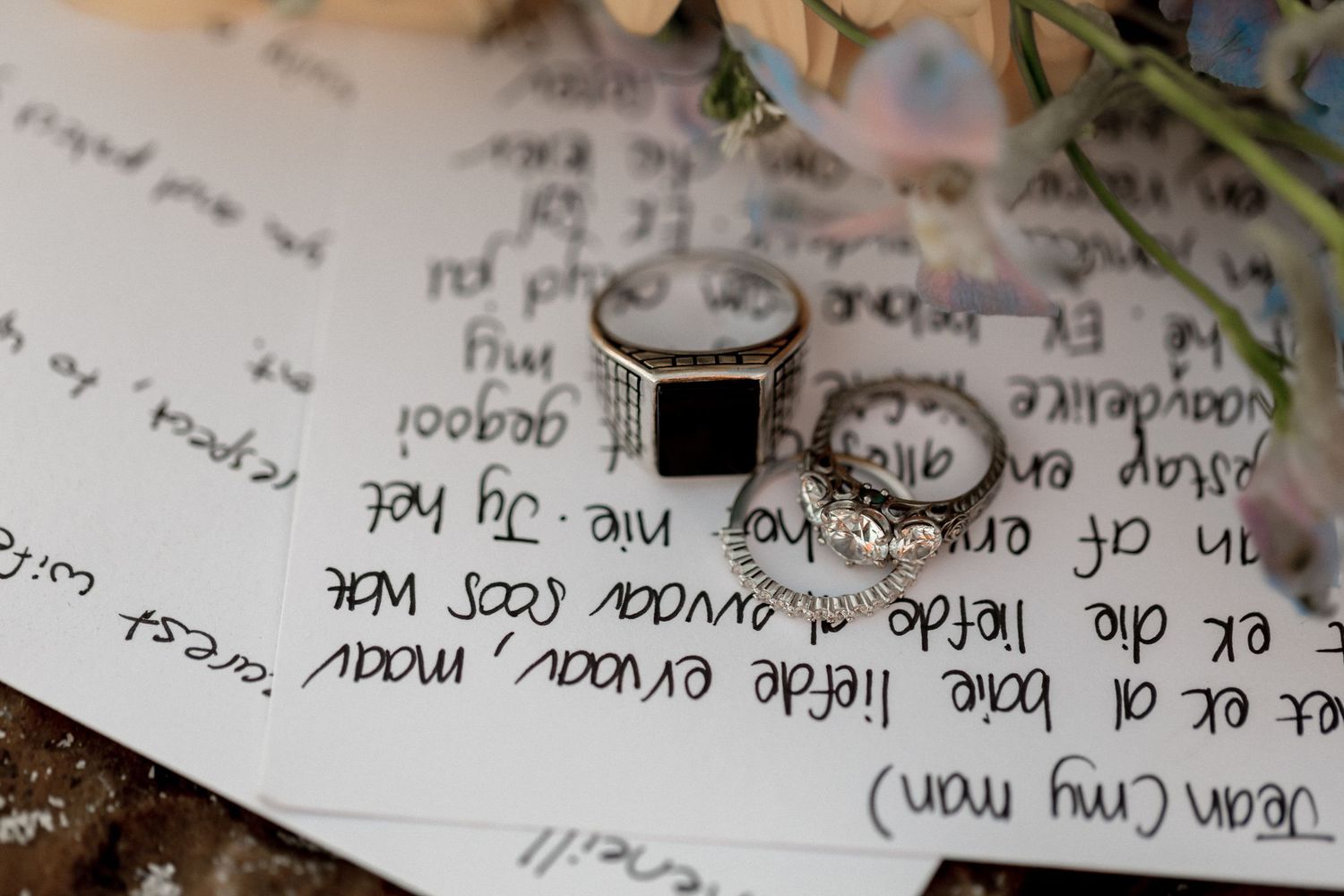 A silver ring with a black stone center lies on handwritten text with floral elements in soft focus.