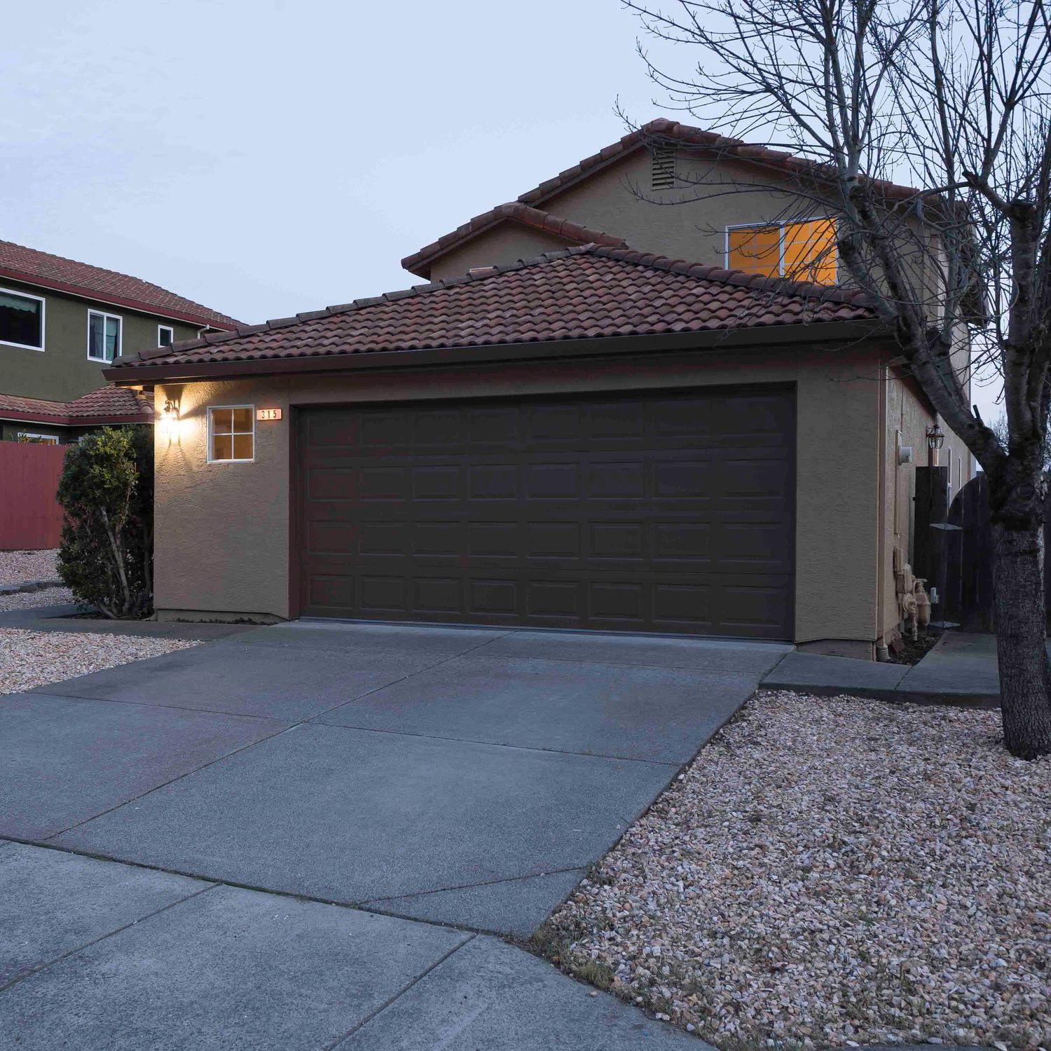 Residential driveway with desert landscaping and attached garage at dusk.