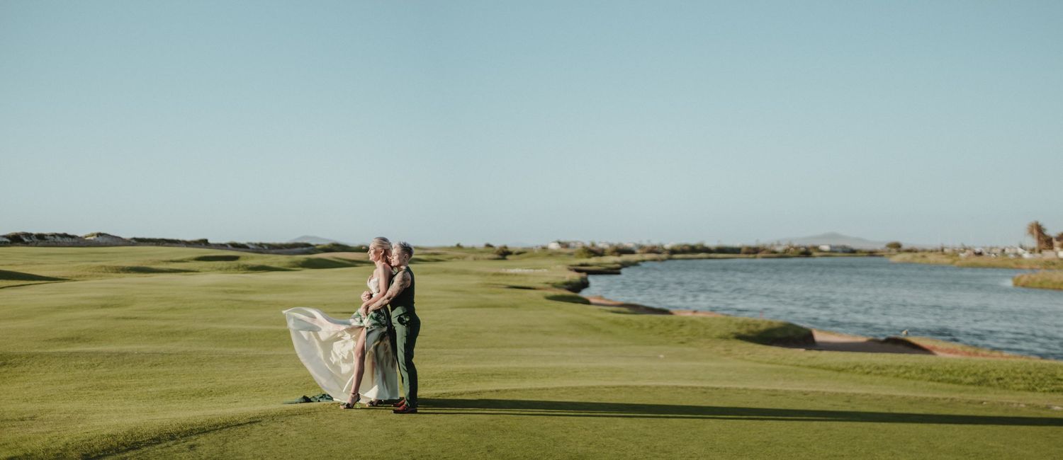 Couple walking together on a scenic coastal golf course with rolling green fairways and ocean views in the distance.