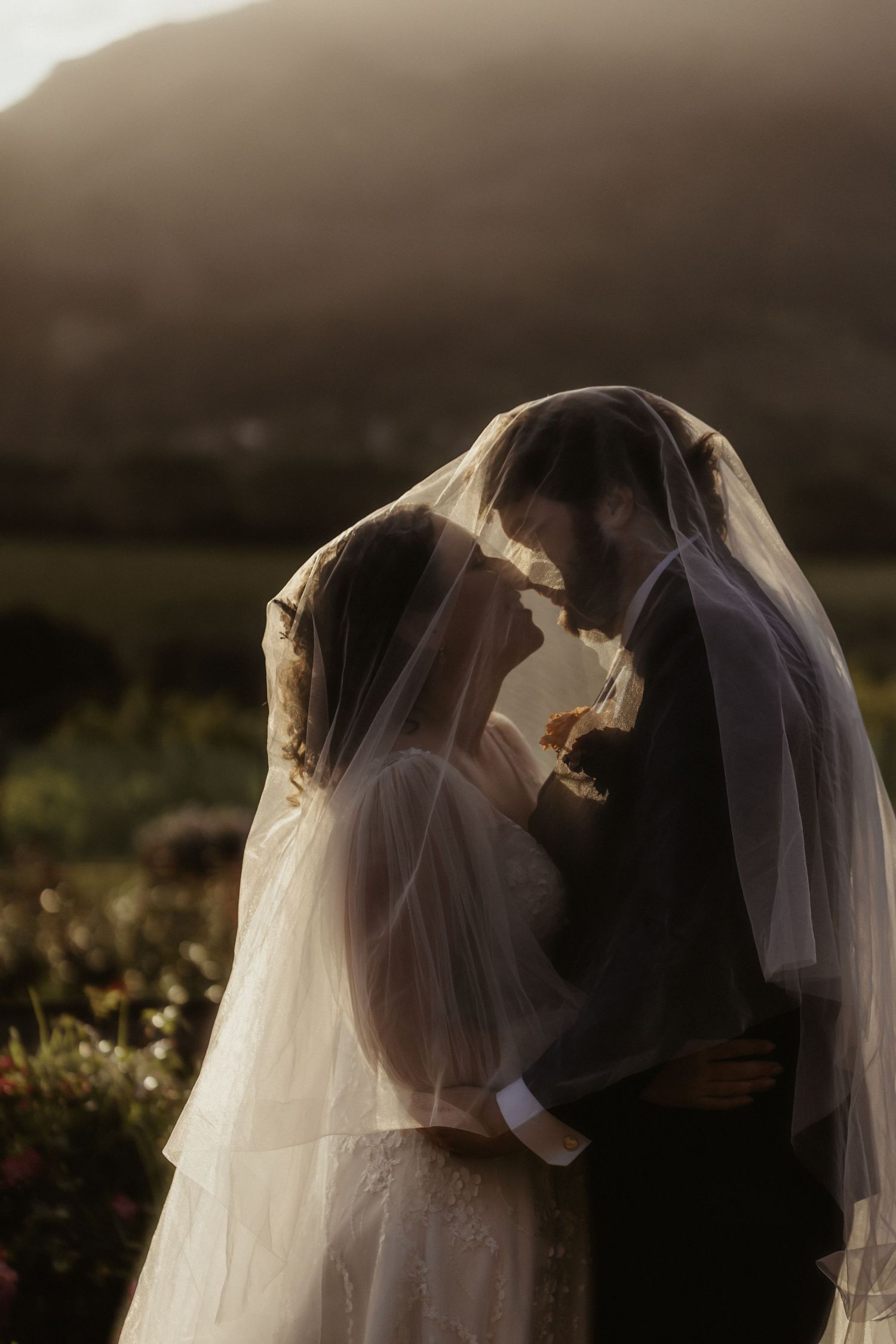 Romantic silhouette of a wedding couple embracing during golden hour in a garden setting.