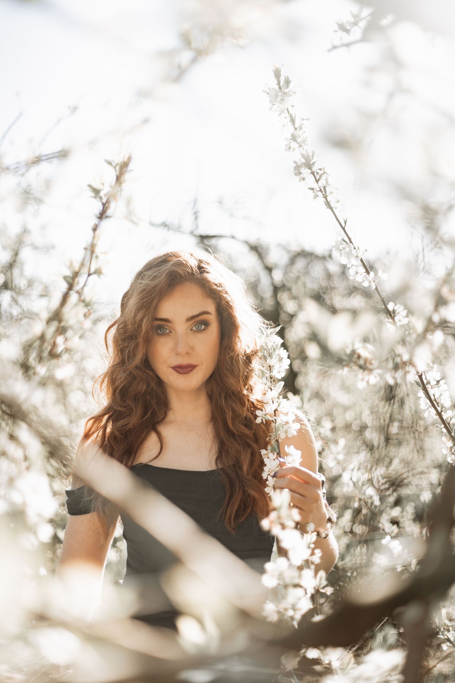 Ethereal portrait in blooming cherry blossoms with soft sunlight creating a dreamy spring atmosphere.
