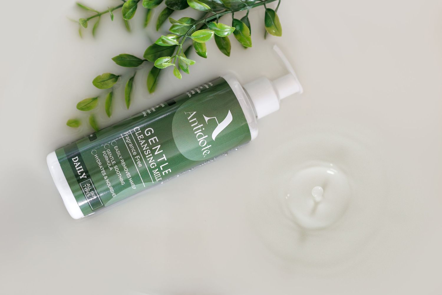 Green beauty product bottles displayed with fresh leafy plant stems against a white background.