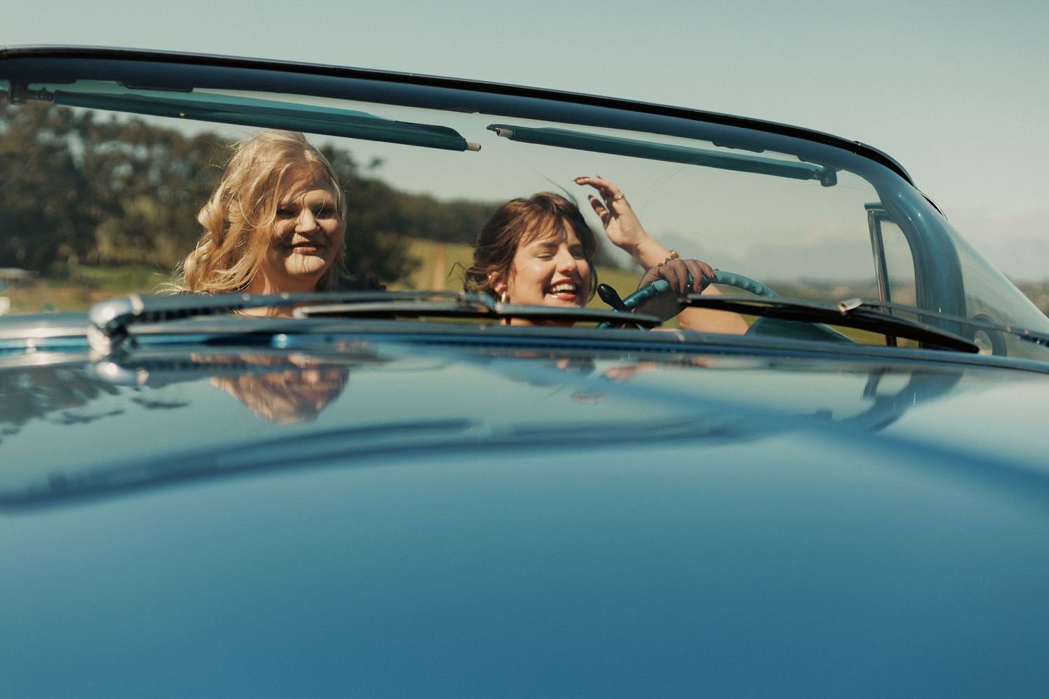 A group of friends enjoy a scenic drive in a convertible car along a coastal road on a sunny day.