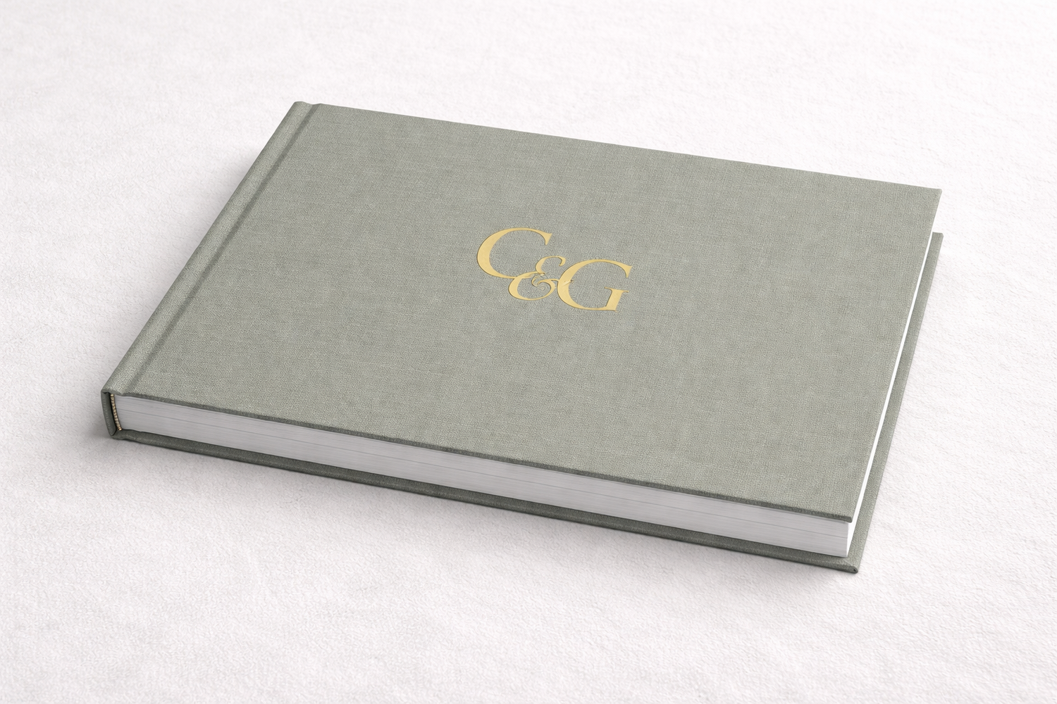 Three elegant gray linen hardcover books with gold foil monogram details lay on a white surface.