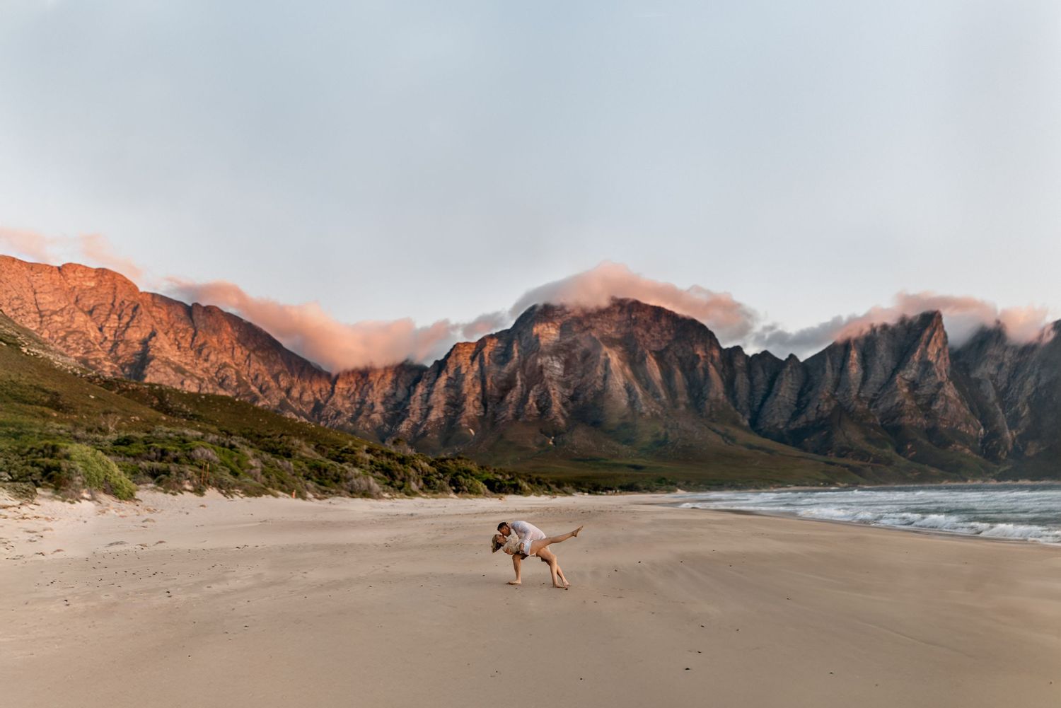 A dog runs along a pristine beach with dramatic mountain cliffs of Kogel Bay, South Africa at sunset.