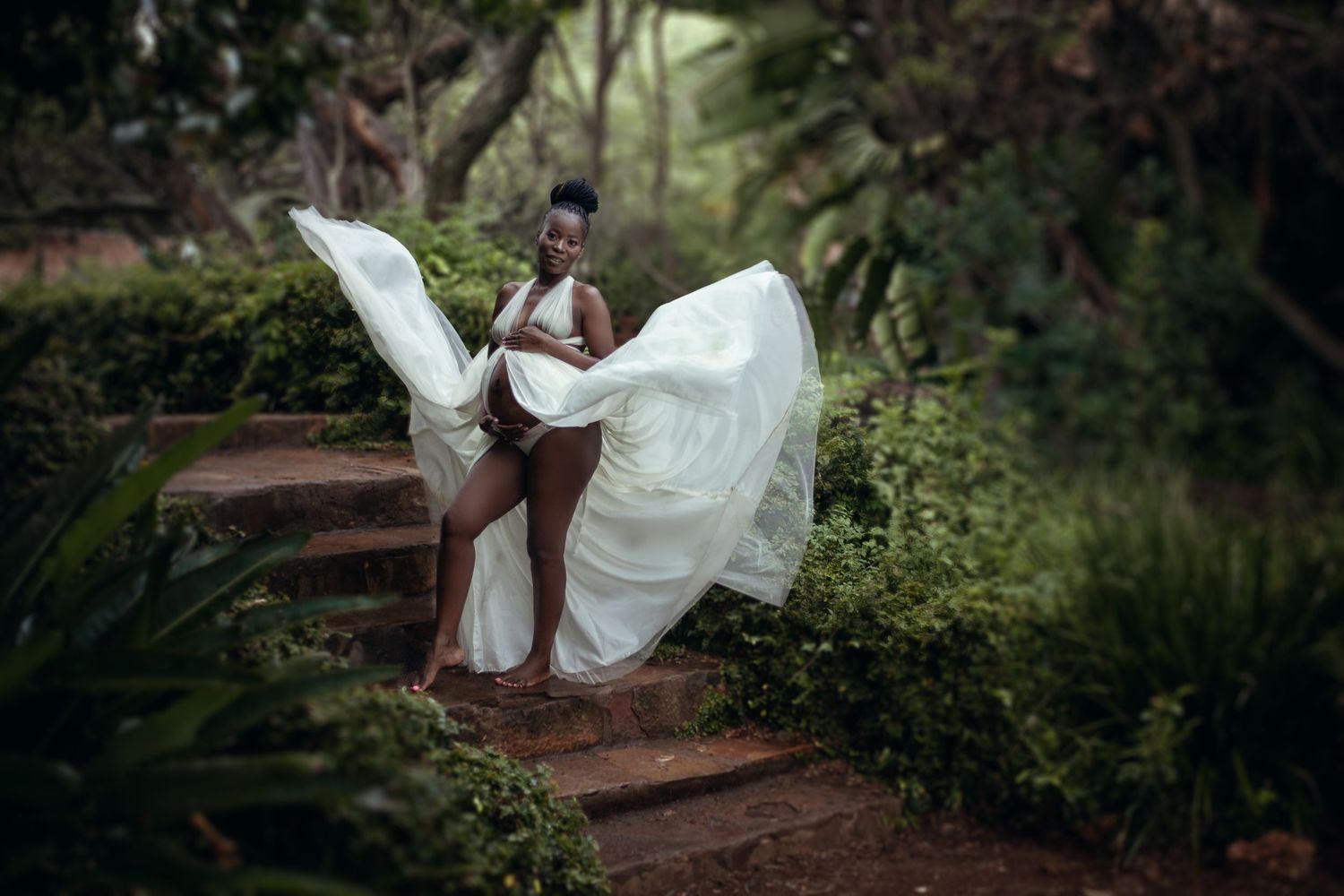 A flowing white dress billows dramatically on garden steps surrounded by lush greenery and natural light.