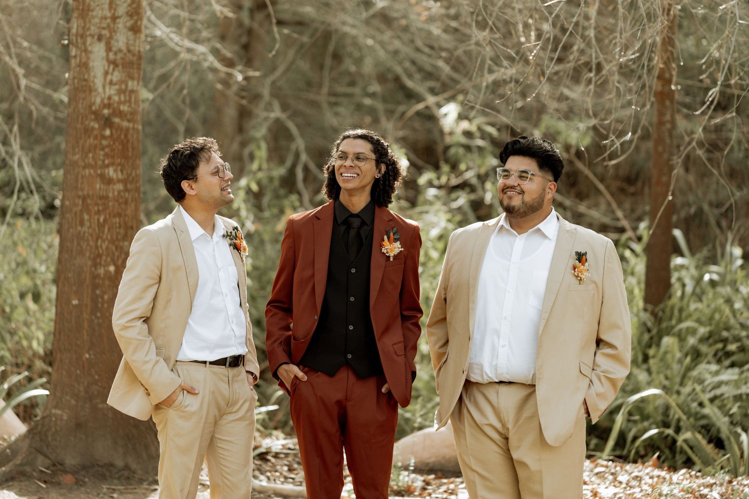 A group in formal attire poses outdoors in a natural setting with cream and burgundy colored clothing.