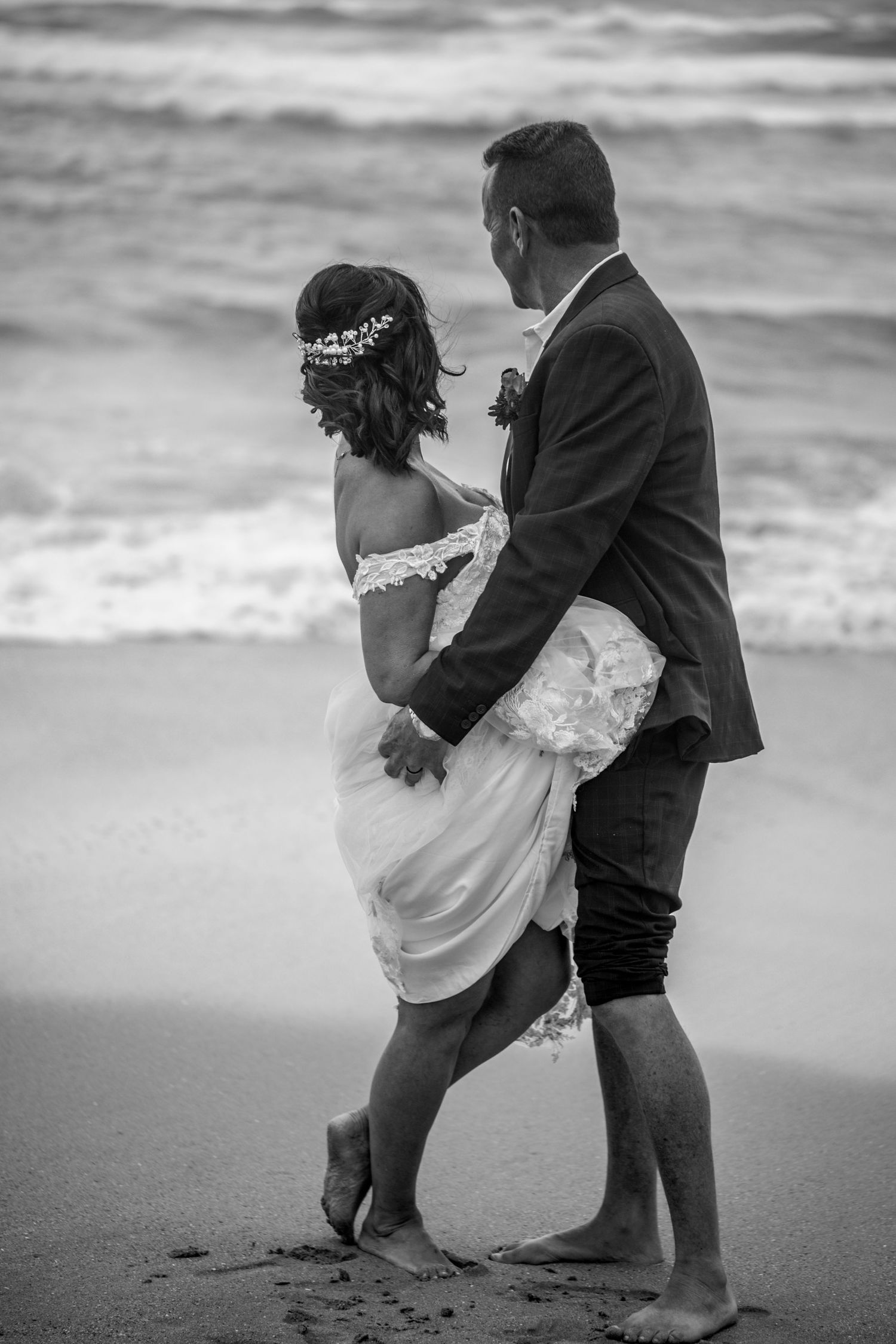 A romantic black and white beach wedding photo showing a couple embracing by the ocean waves.