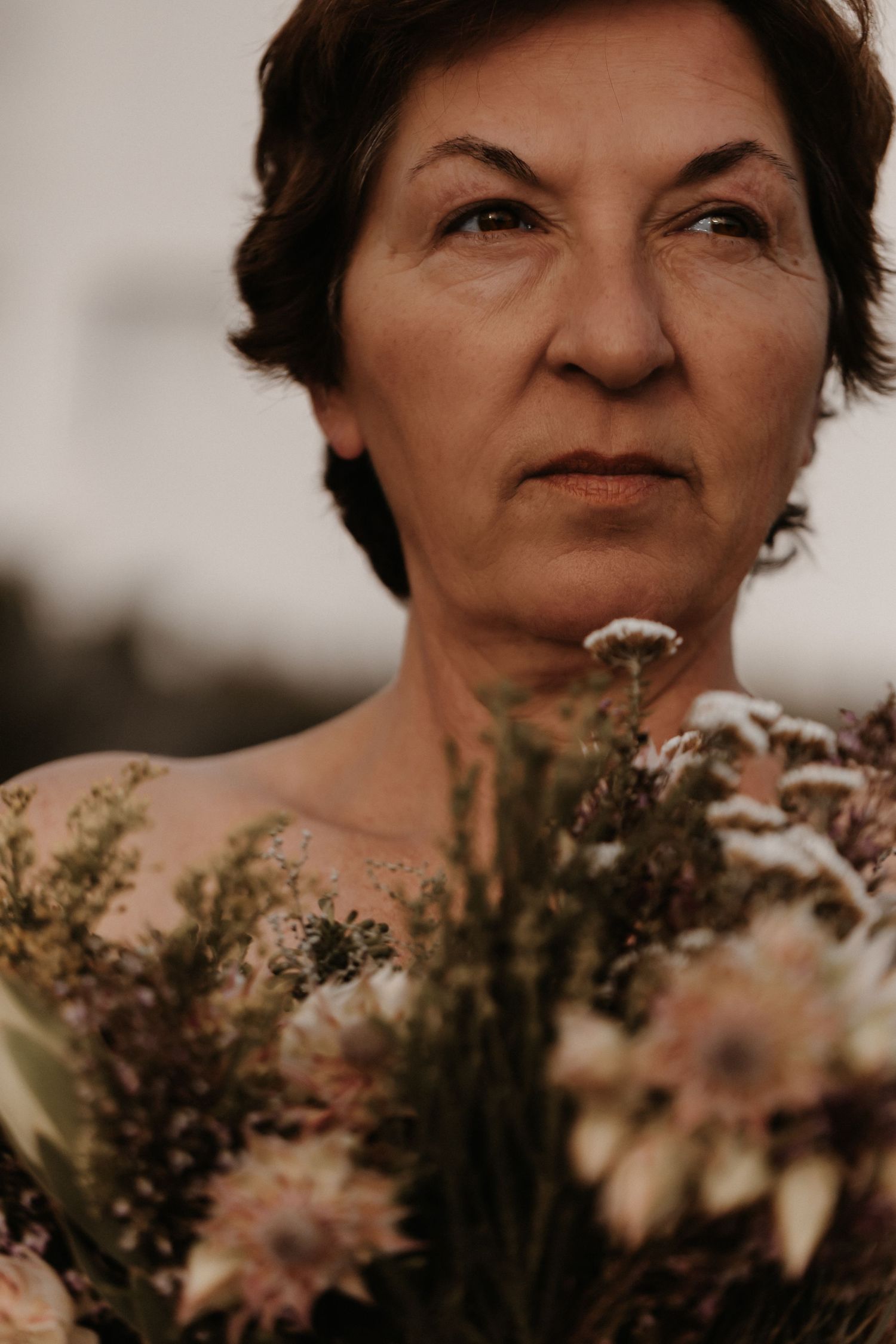 A close-up portrait shows a person with short dark hair holding flowers at sunset in warm sepia tones.