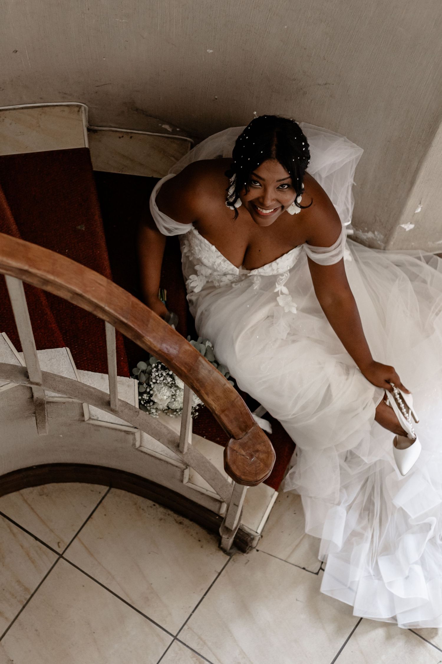 A wedding dress trailing down an elegant curved wooden staircase with tile flooring below.