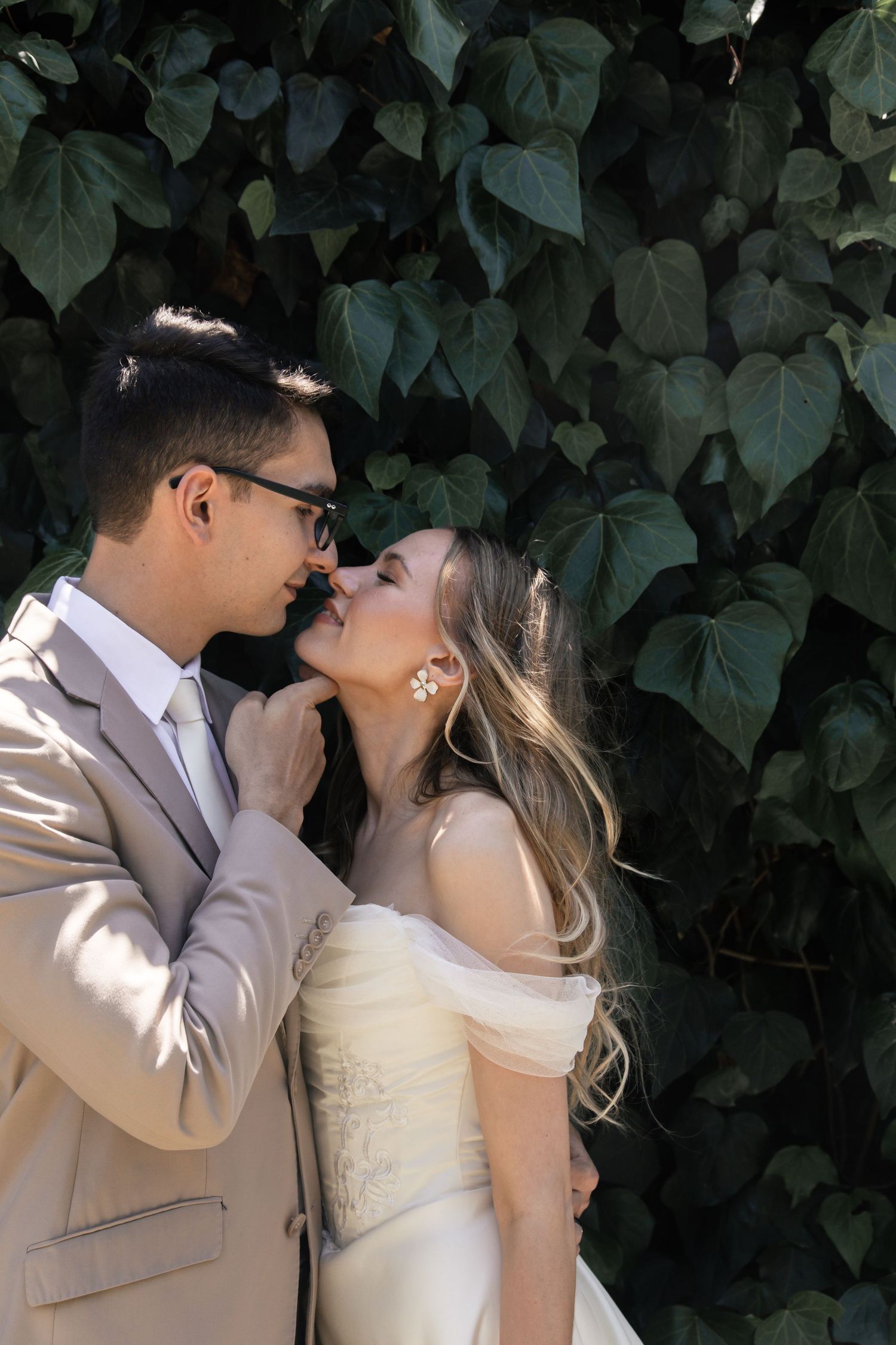 A couple shares intimate wedding moments against a backdrop of lush green ivy leaves.