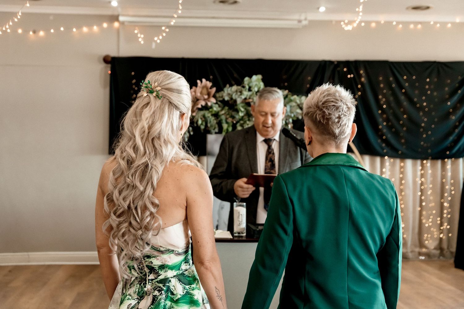 Wedding celebration showing people in formal attire and emerald green outfits mingling at an indoor venue.