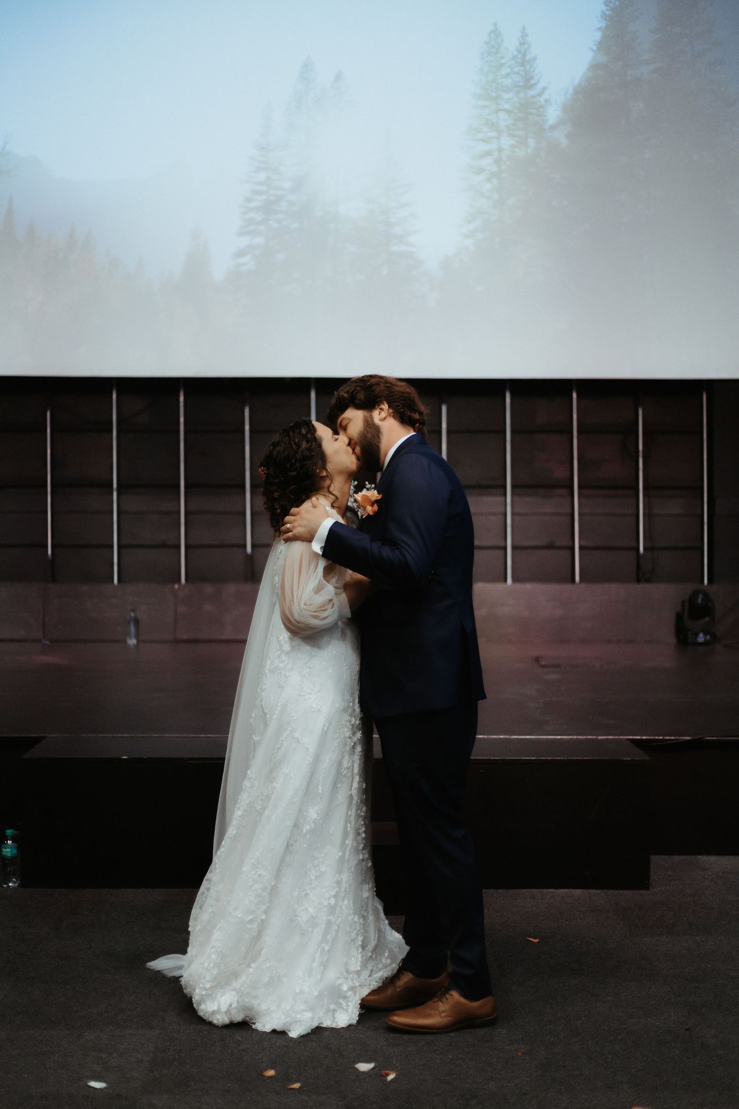 A couple in wedding attire share an intimate dance dip against a dark rustic wall.