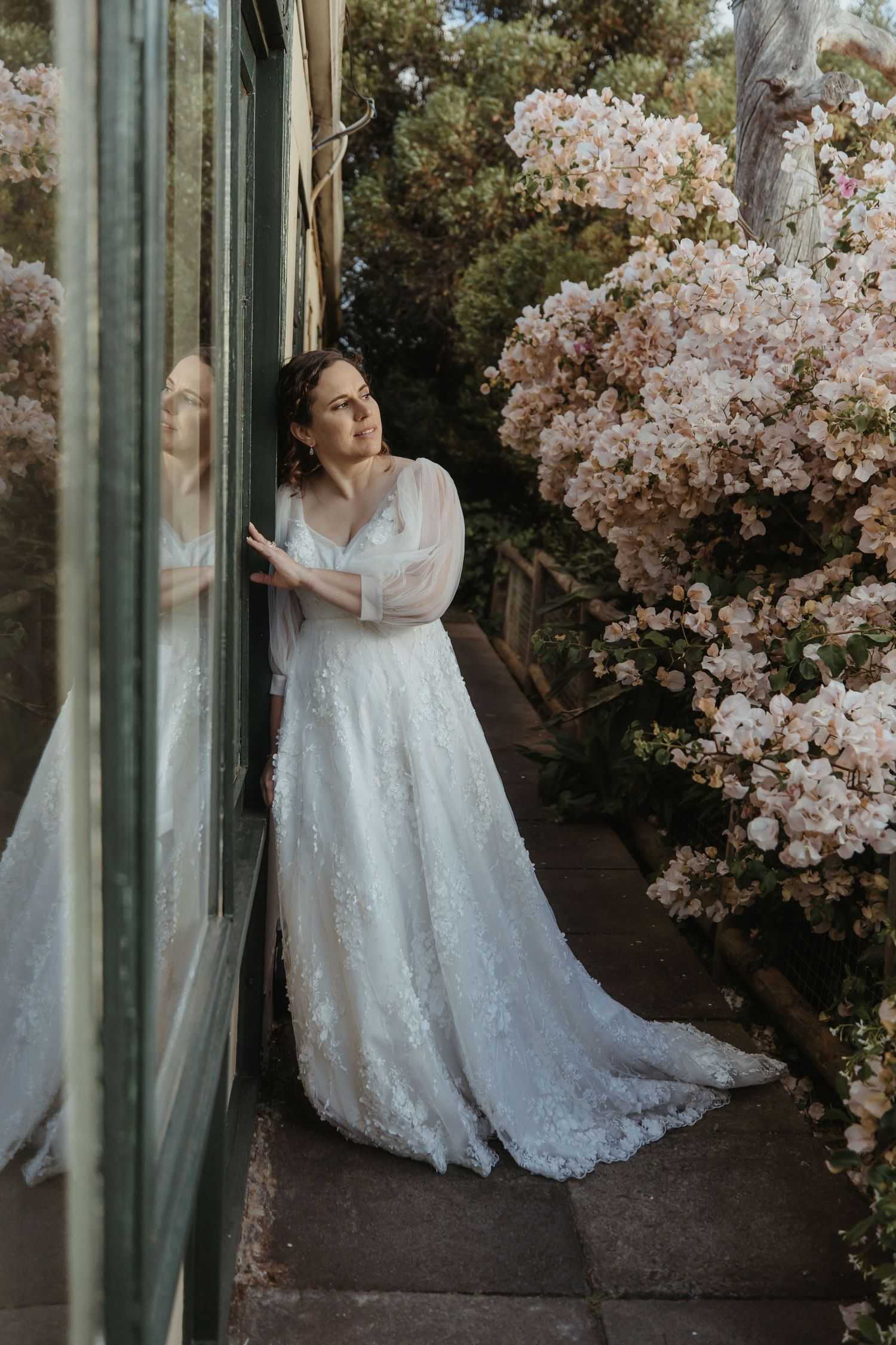 A romantic wedding scene with a white lace gown against flowering cherry blossoms and green columns outdoors.