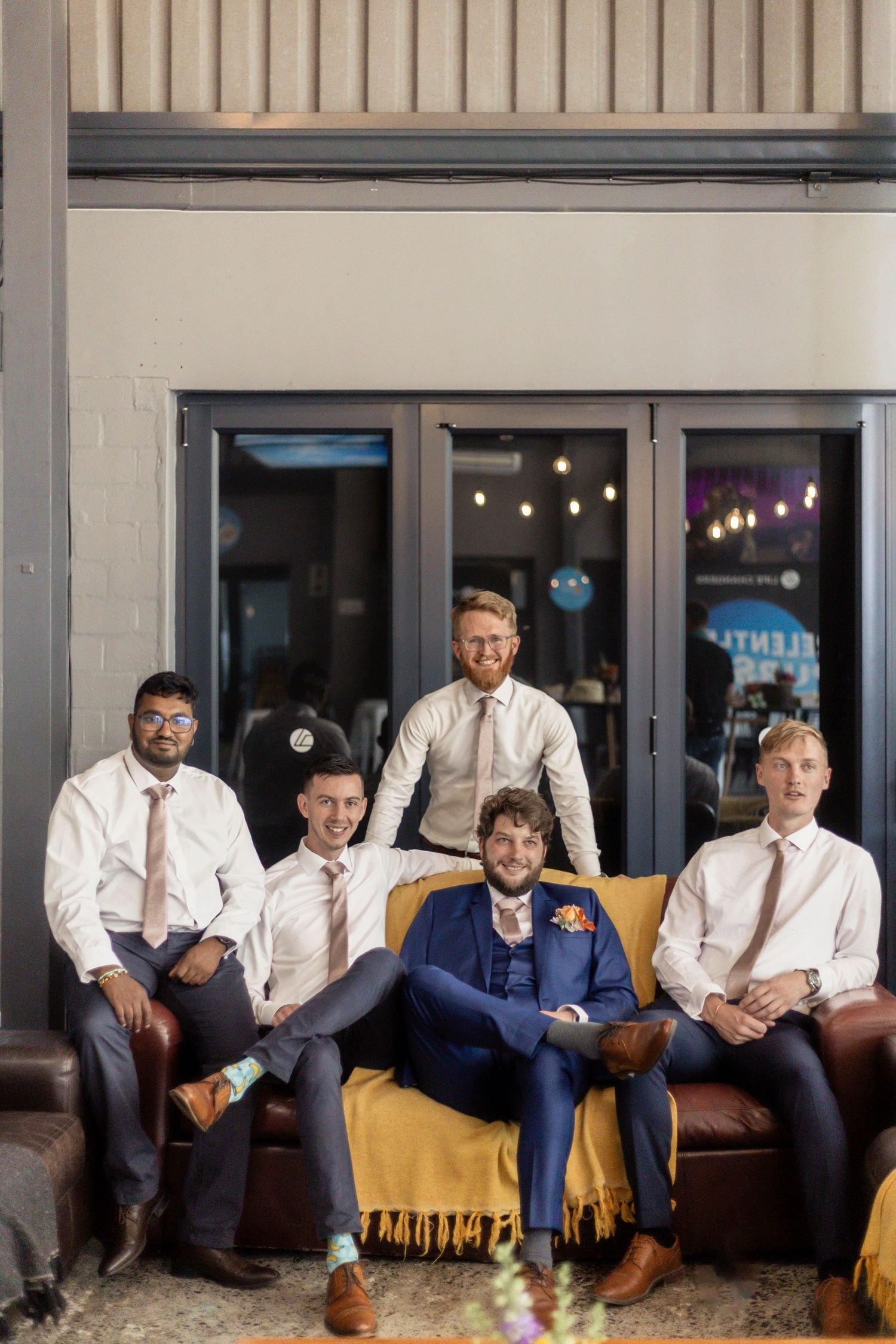 A group sits casually on a brown leather couch in coordinated white shirts and navy attire during a photo session.