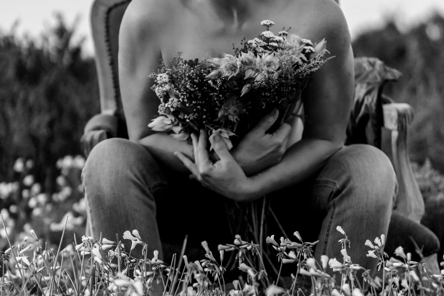 Artistic black and white photograph showing hands holding delicate wildflowers while sitting in a blooming meadow.