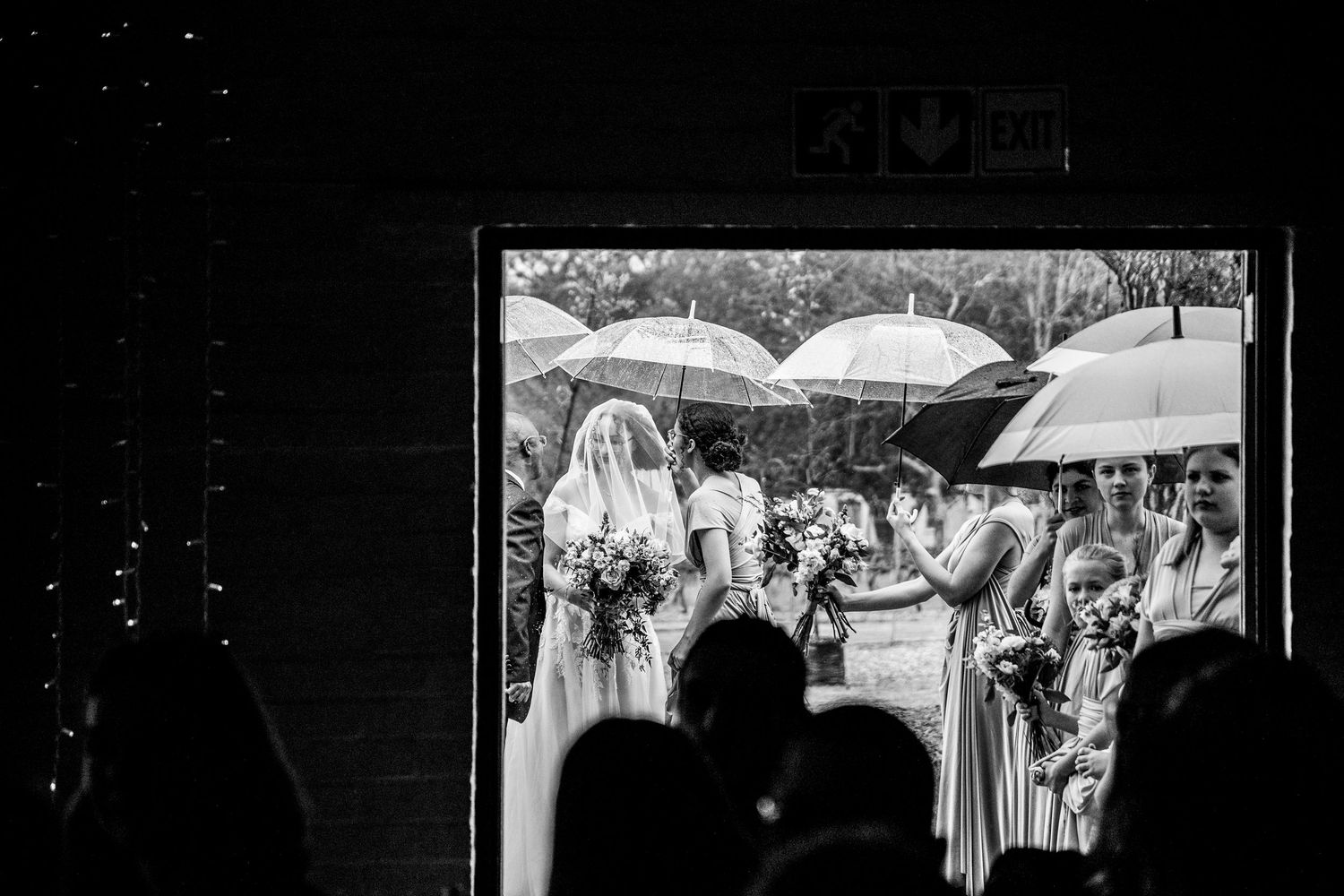 A black and white scene of people with white umbrellas gathered outdoors during a rainy ceremony.