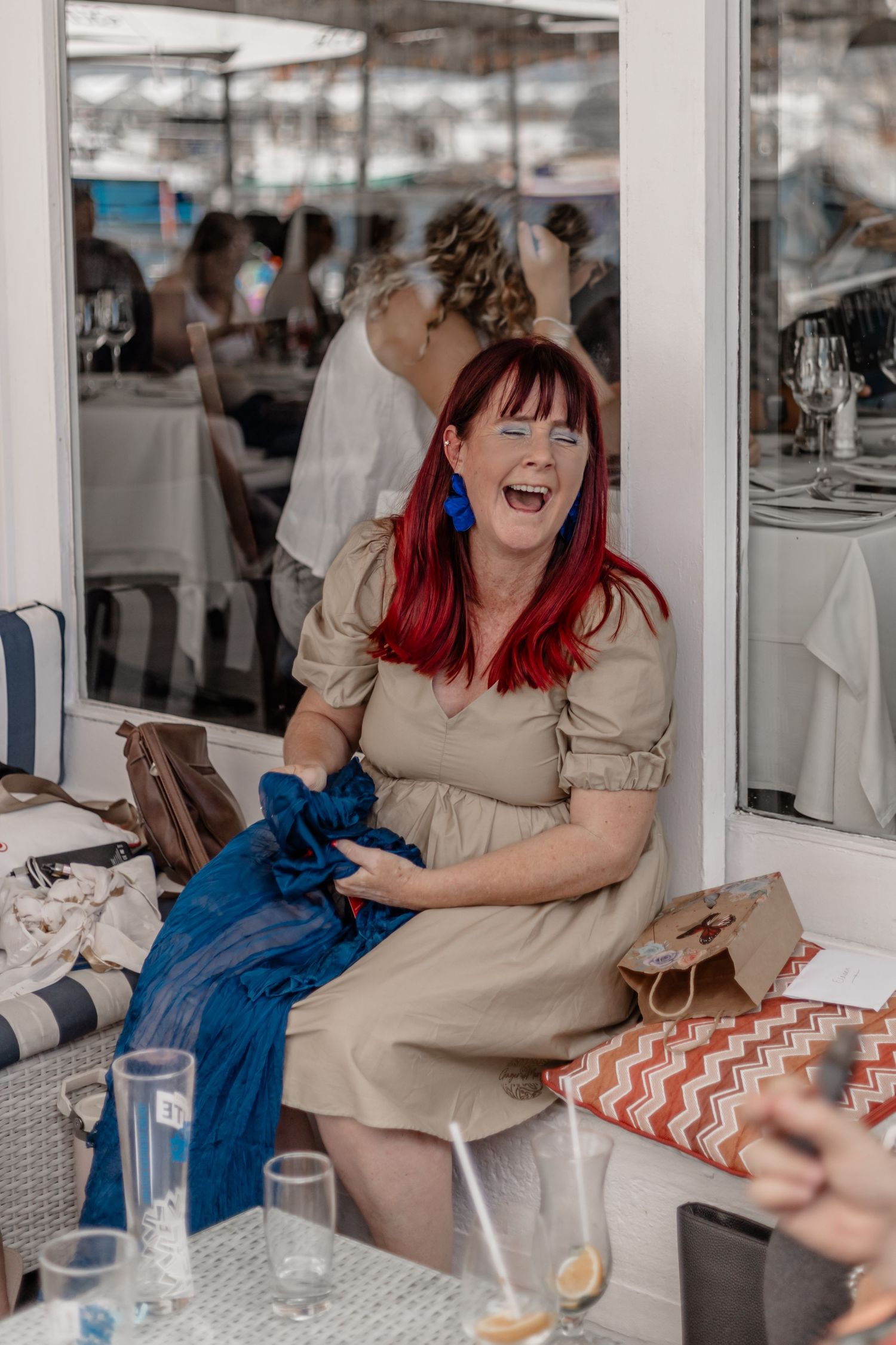 Someone with bright red hair and a beige dress laughs joyfully while sitting at a table during what appears to be a celebration.