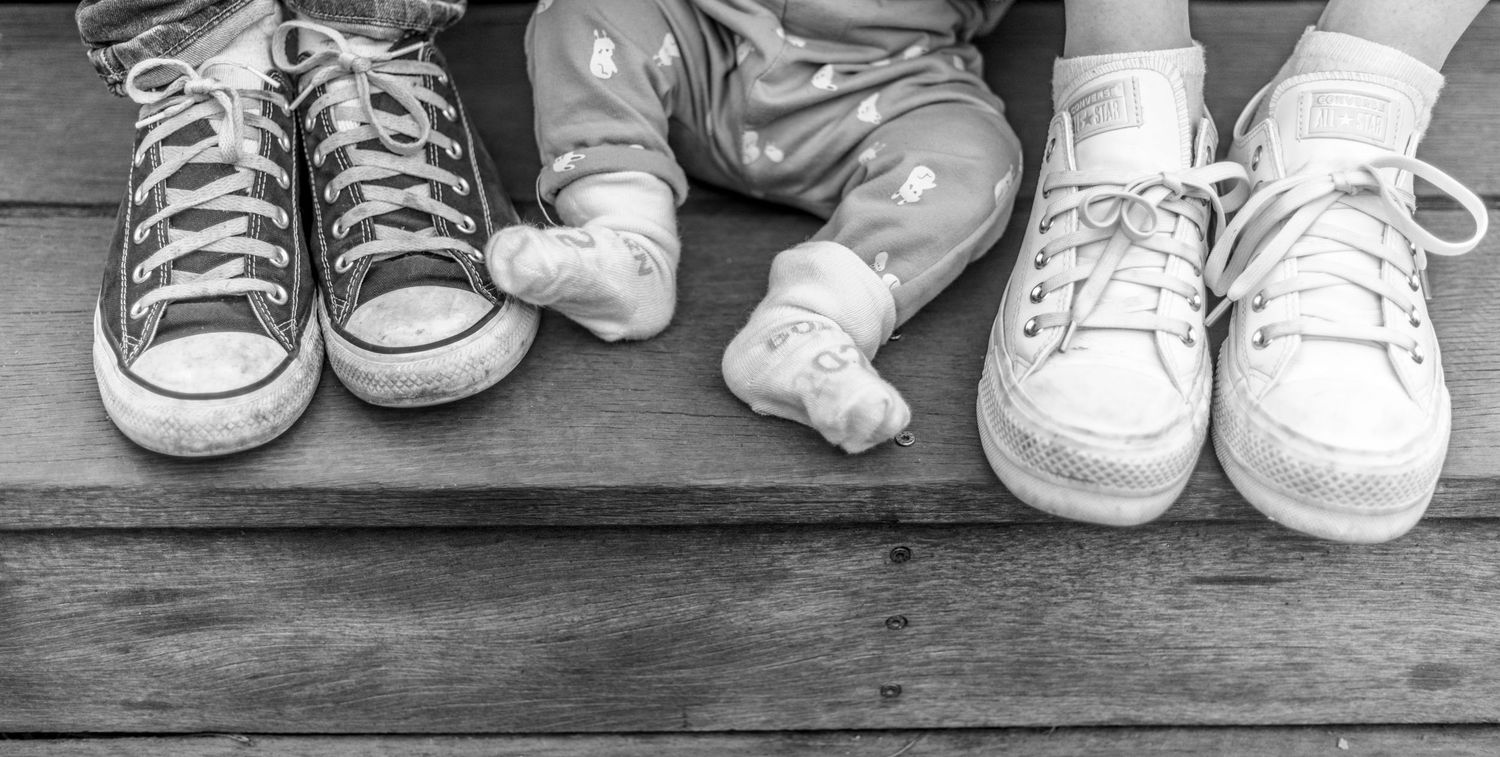 A collection of sneakers and shoes arranged in a row showing different styles and sizes on a wooden surface.