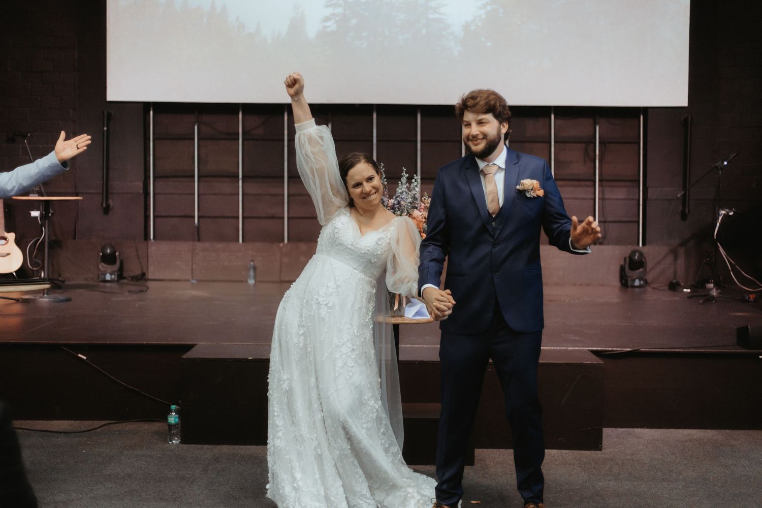 A couple in formal wedding attire celebrates with joyful dance moves during their reception.
