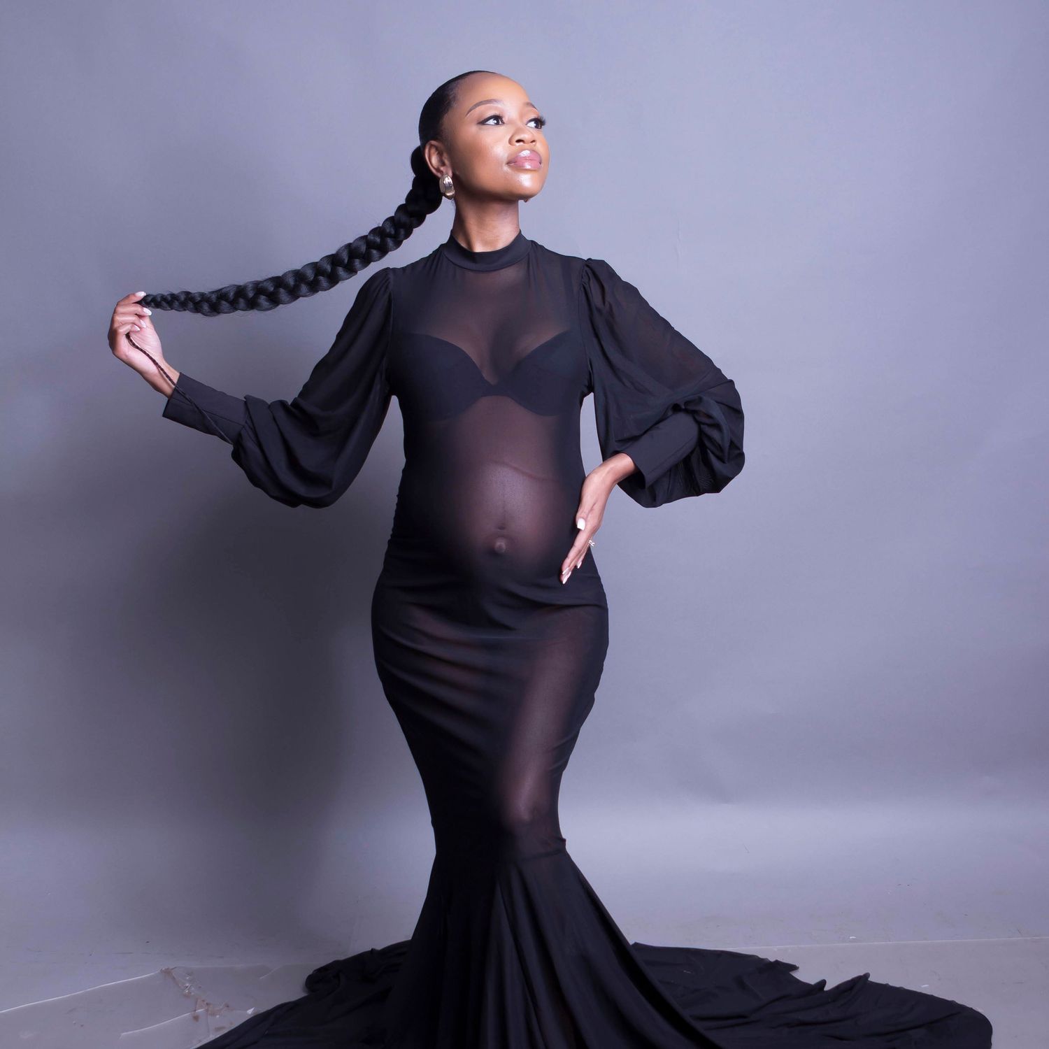 Maternity photo of an expectant mother in a sheer black gown with long braided hair.