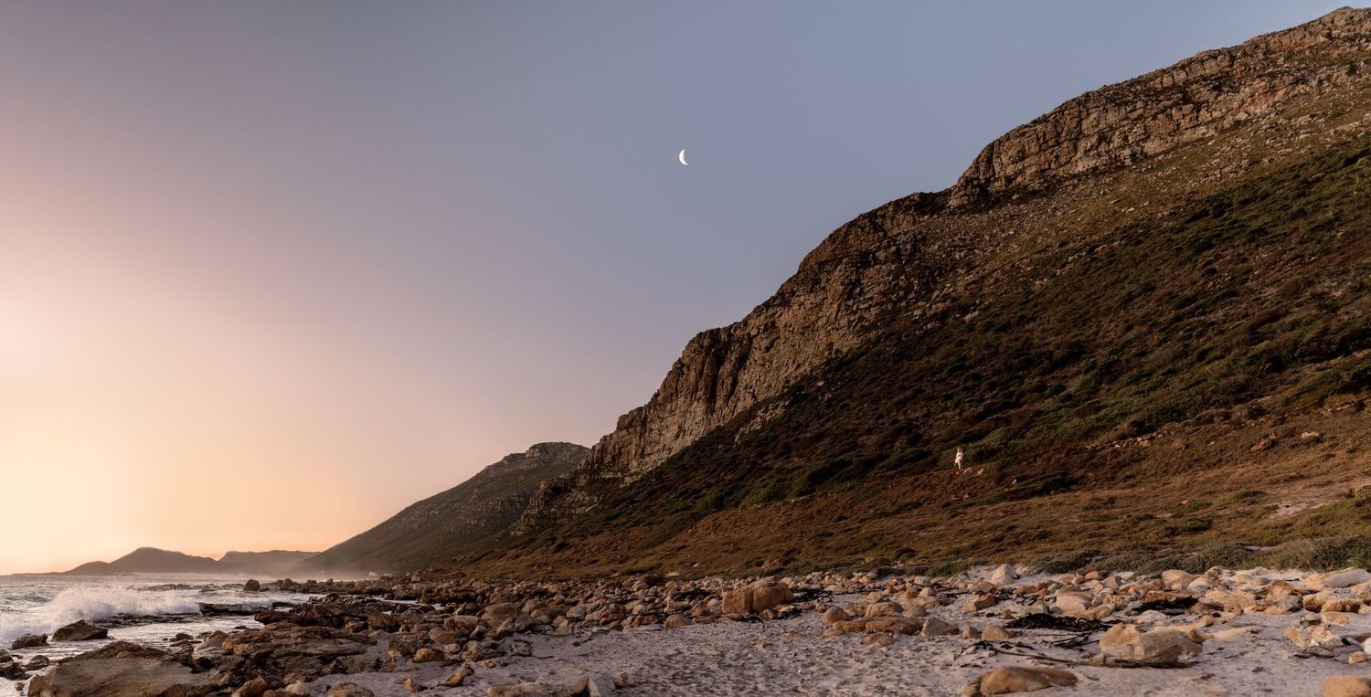 A scenic panoramic view of a coastal mountain landscape at sunset with rocky cliffs meeting the ocean.