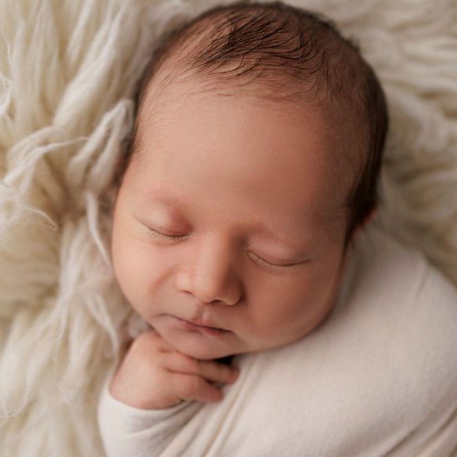 Peaceful sleeping newborn baby photographed on cream colored fabric.
