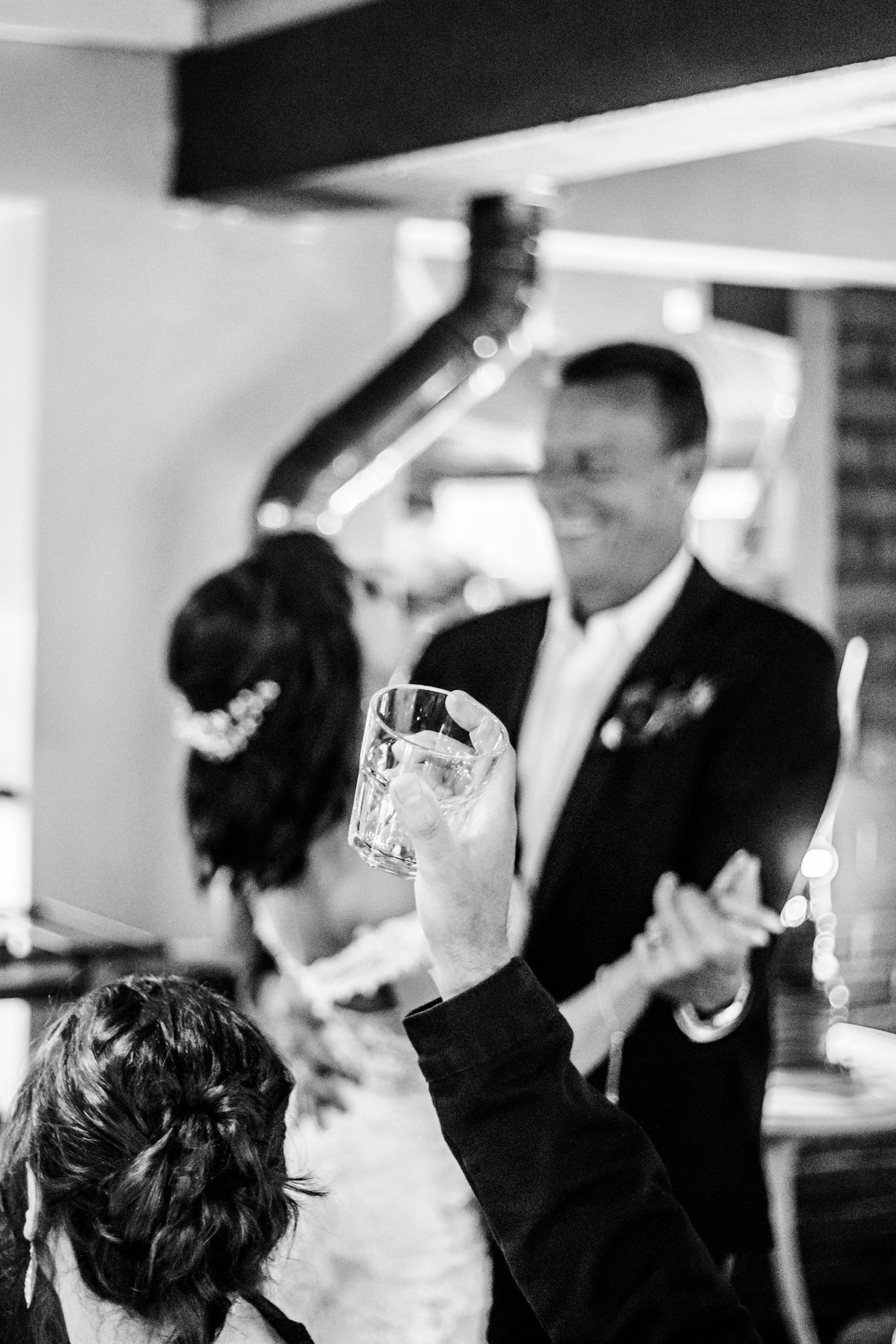 A black and white candid wedding reception photo showing guests socializing and holding drinks during a celebration.