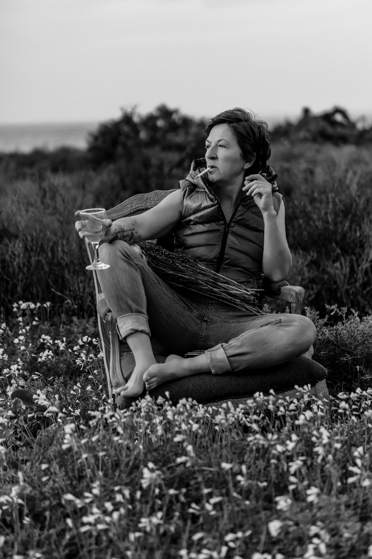 Person sits cross-legged in a wildflower meadow wearing casual attire in black and white photography.