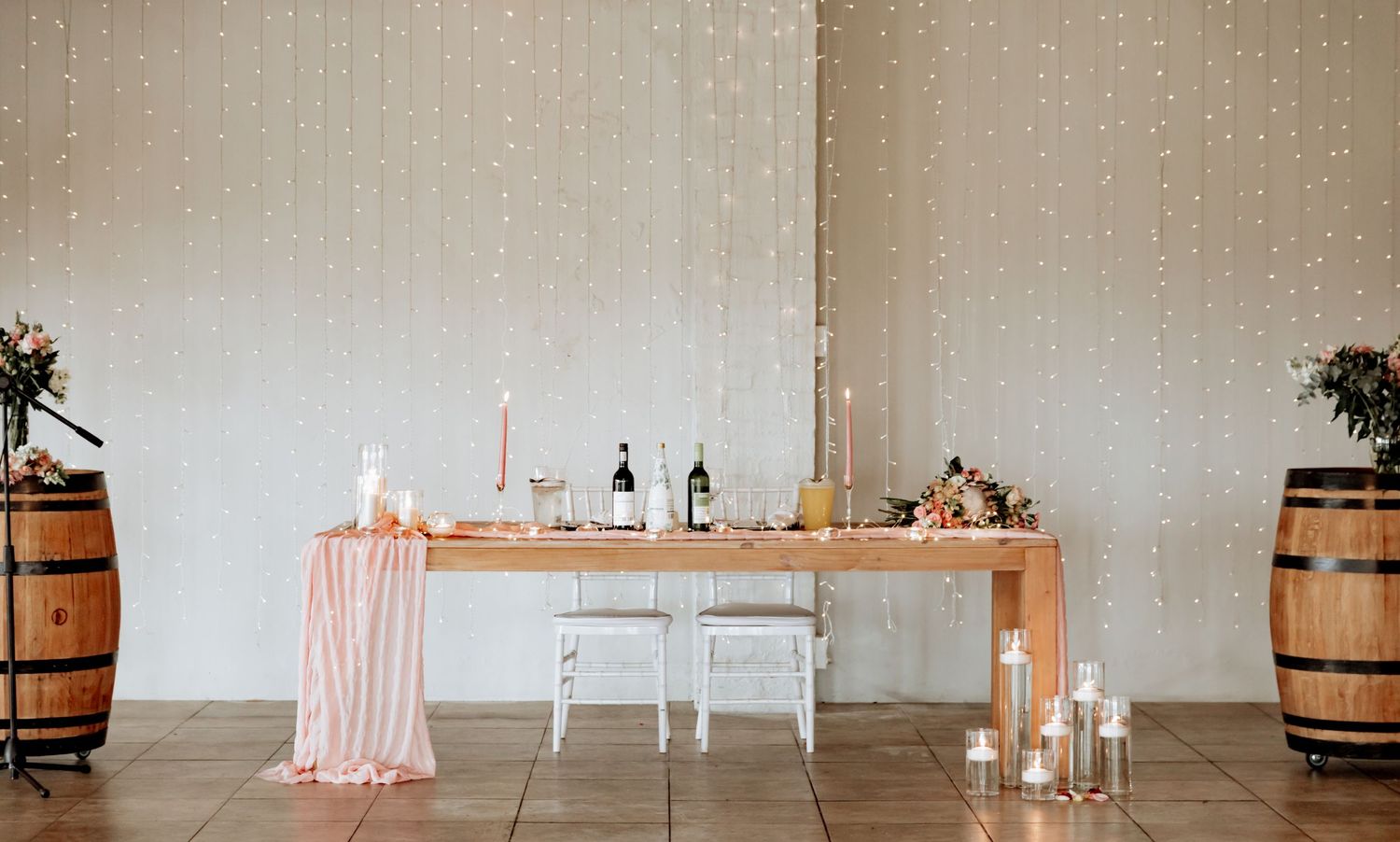 Rustic barrels and peach-colored drapery create an ethereal wedding ceremony setup in a minimalist industrial space.