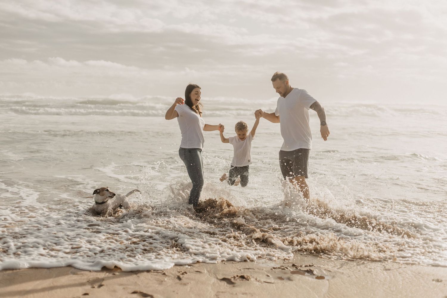 A group plays and splashes together in the ocean waves along a scenic beach at sunset.