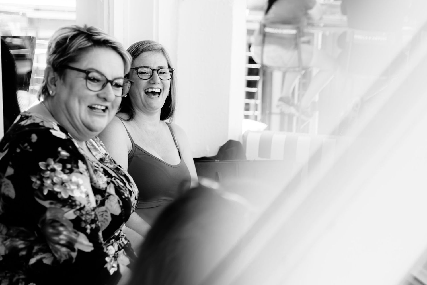 Two women in glasses share a joyful laugh together in black and white photography.