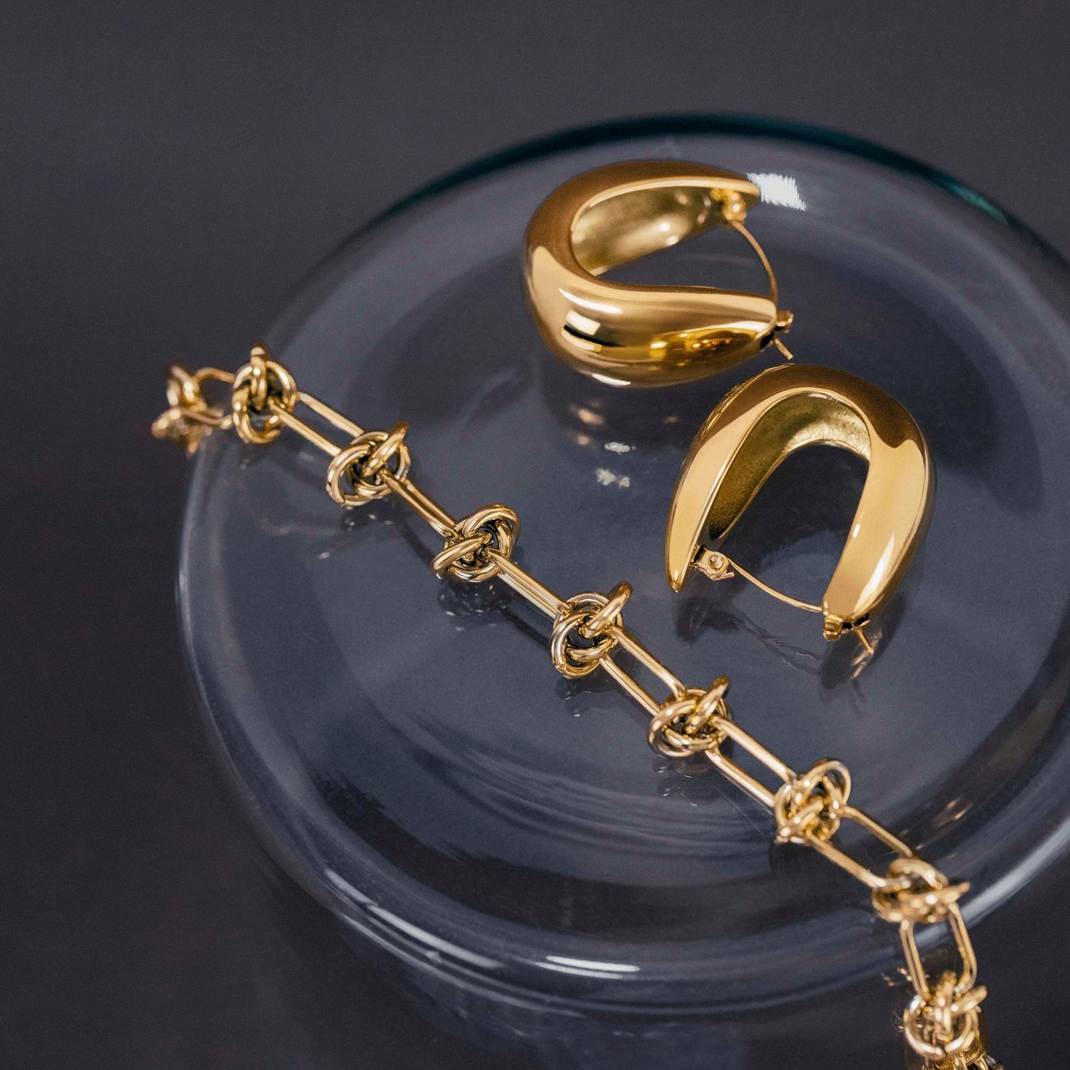 Gold jewelry pieces including chain bracelet and curved accessories displayed on clear surface.