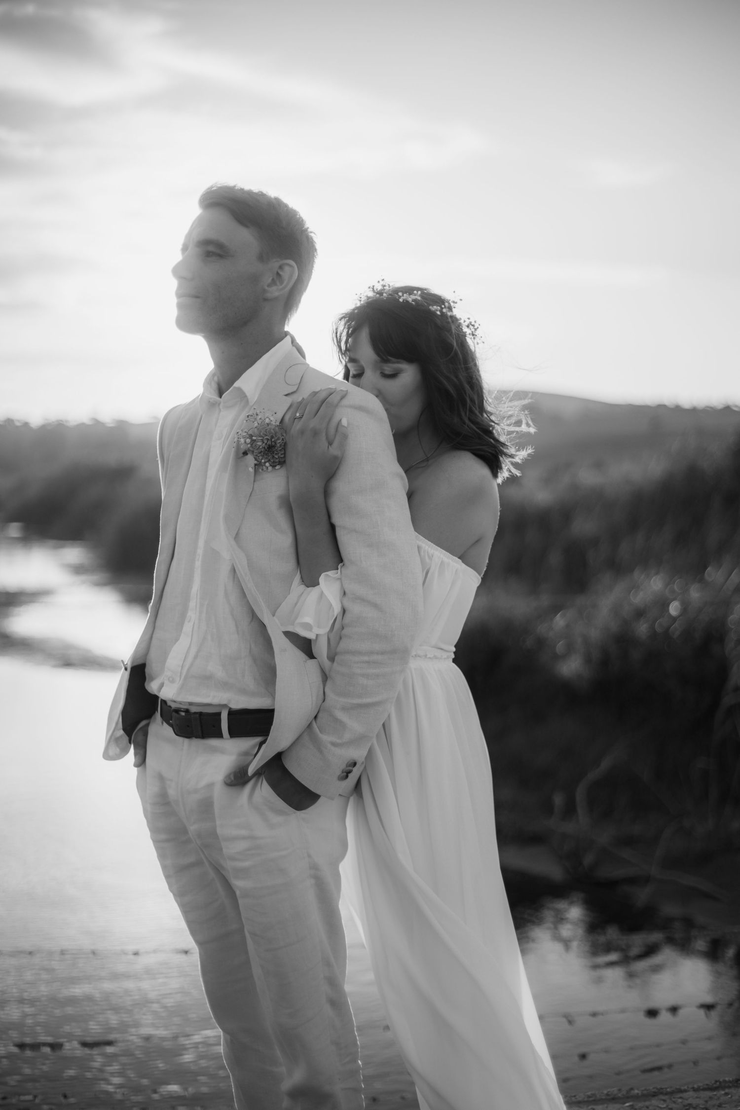 A romantic black and white wedding photo shows a couple embracing on a beach at sunset.