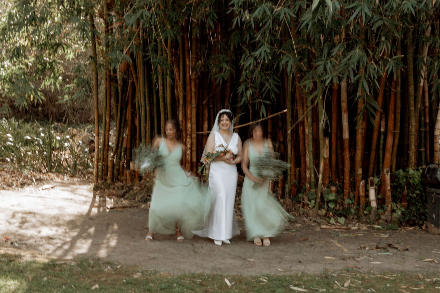 Group in white dresses poses in front of a dark bamboo grove for outdoor forest photography session.