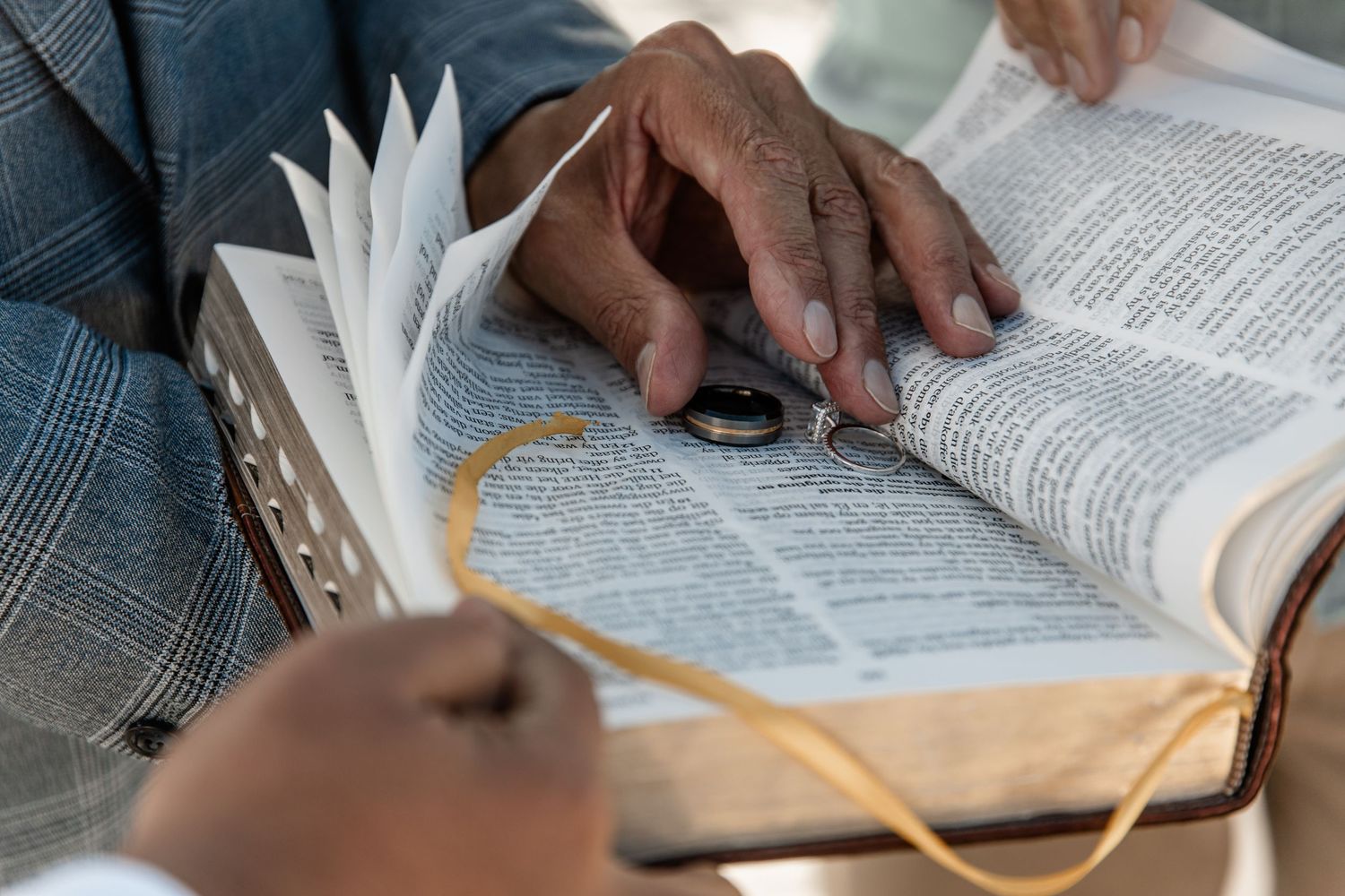 Close-up view of hands holding and reading an open text book with a yellow bookmark ribbon.