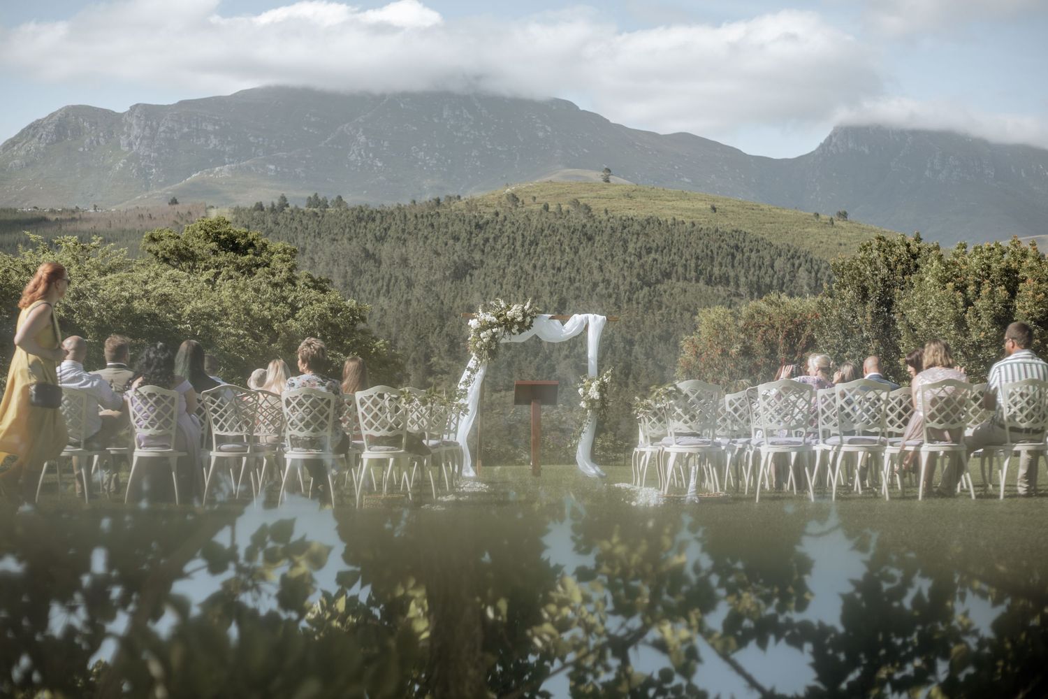 Mountain panorama reflected in calm lake waters with trees and clouds creating a mirror-like symmetrical effect.