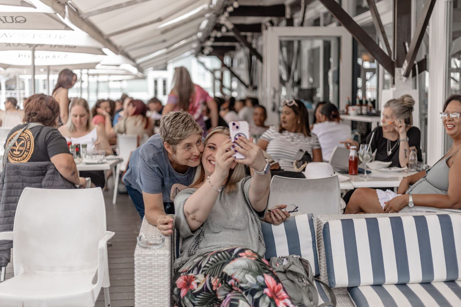 People gather at an outdoor cafe terrace enjoying drinks and conversation on a sunny day.
