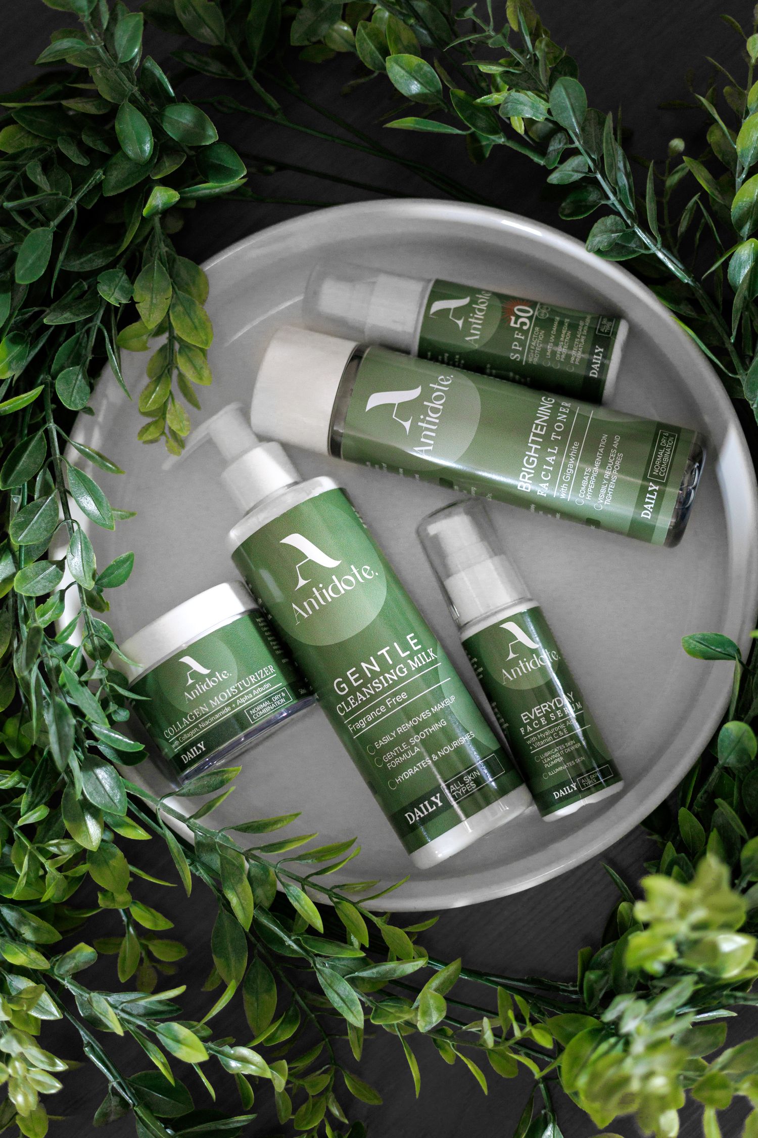 Green skincare products displayed in a white ceramic bowl surrounded by lush foliage and natural greenery.