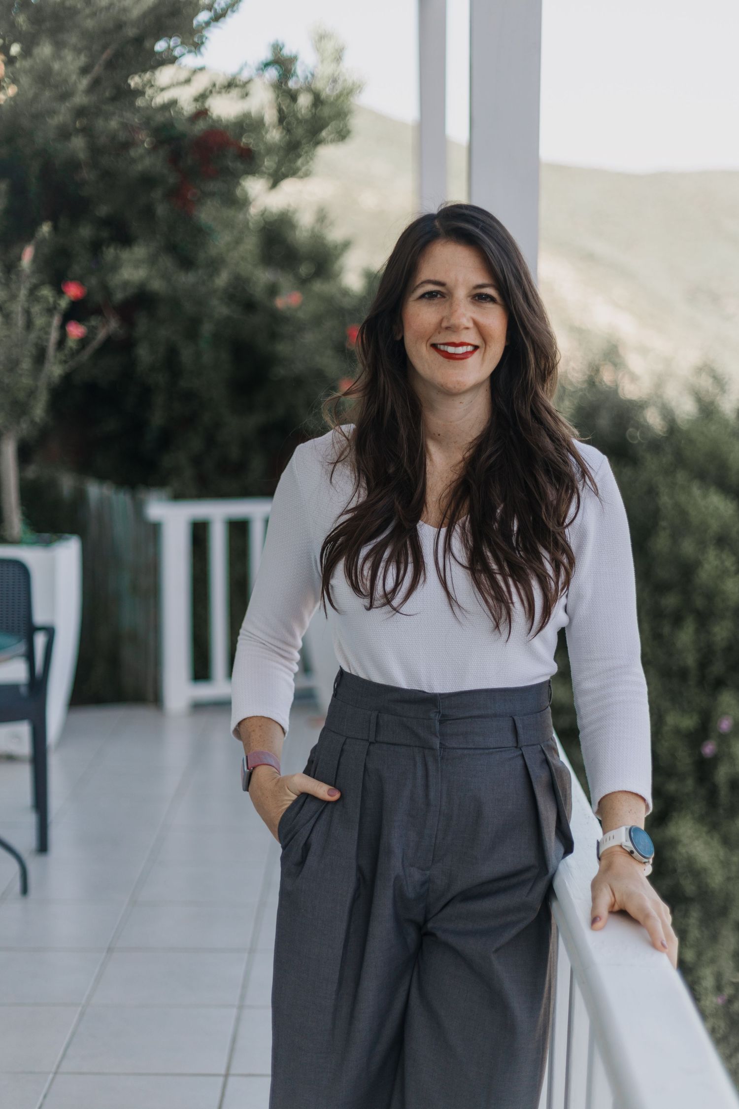 Professional lifestyle portrait on outdoor patio featuring white blouse and high-waisted gray trousers in natural lighting.