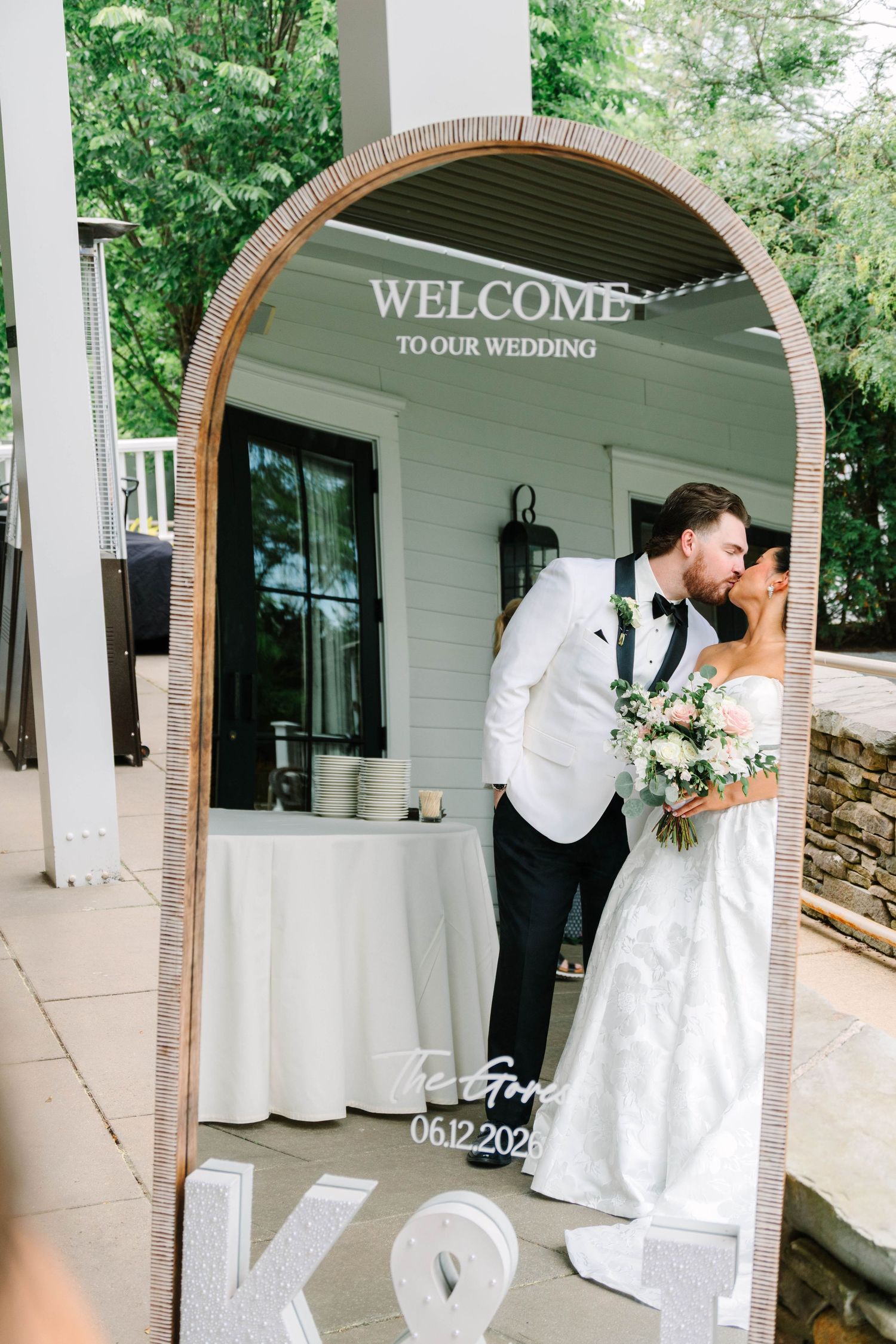 Newlyweds share a kiss reflected in a welcome wedding mirror sign dated 06.12.2024.
