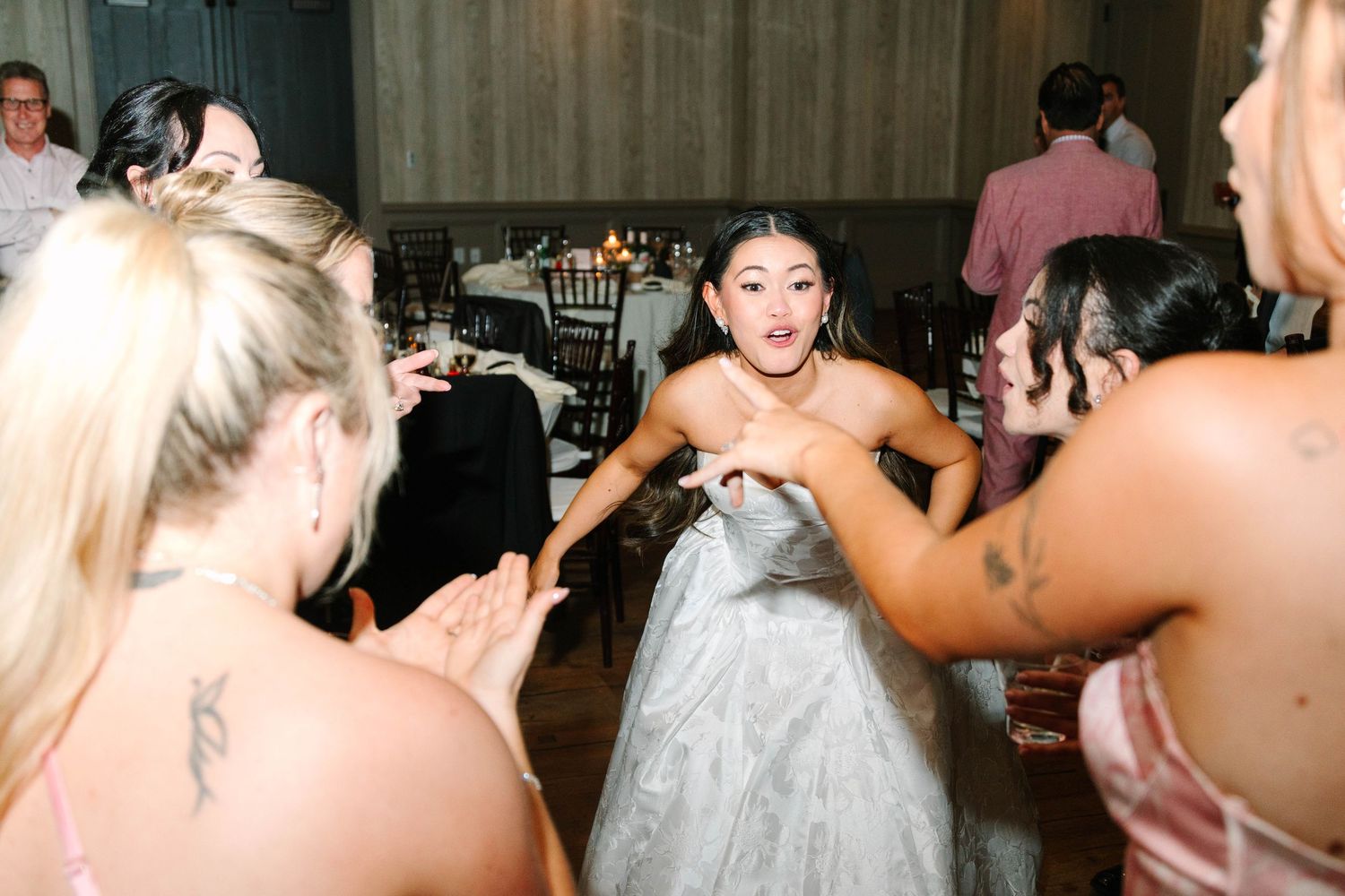 Bride in white gown dancing and interacting with guests at lively wedding reception.