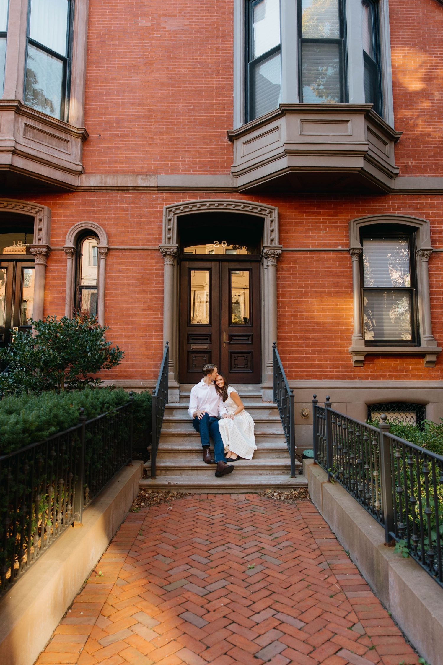 Couple in wedding attire embracing on brick steps of a classic Boston brownstone building.