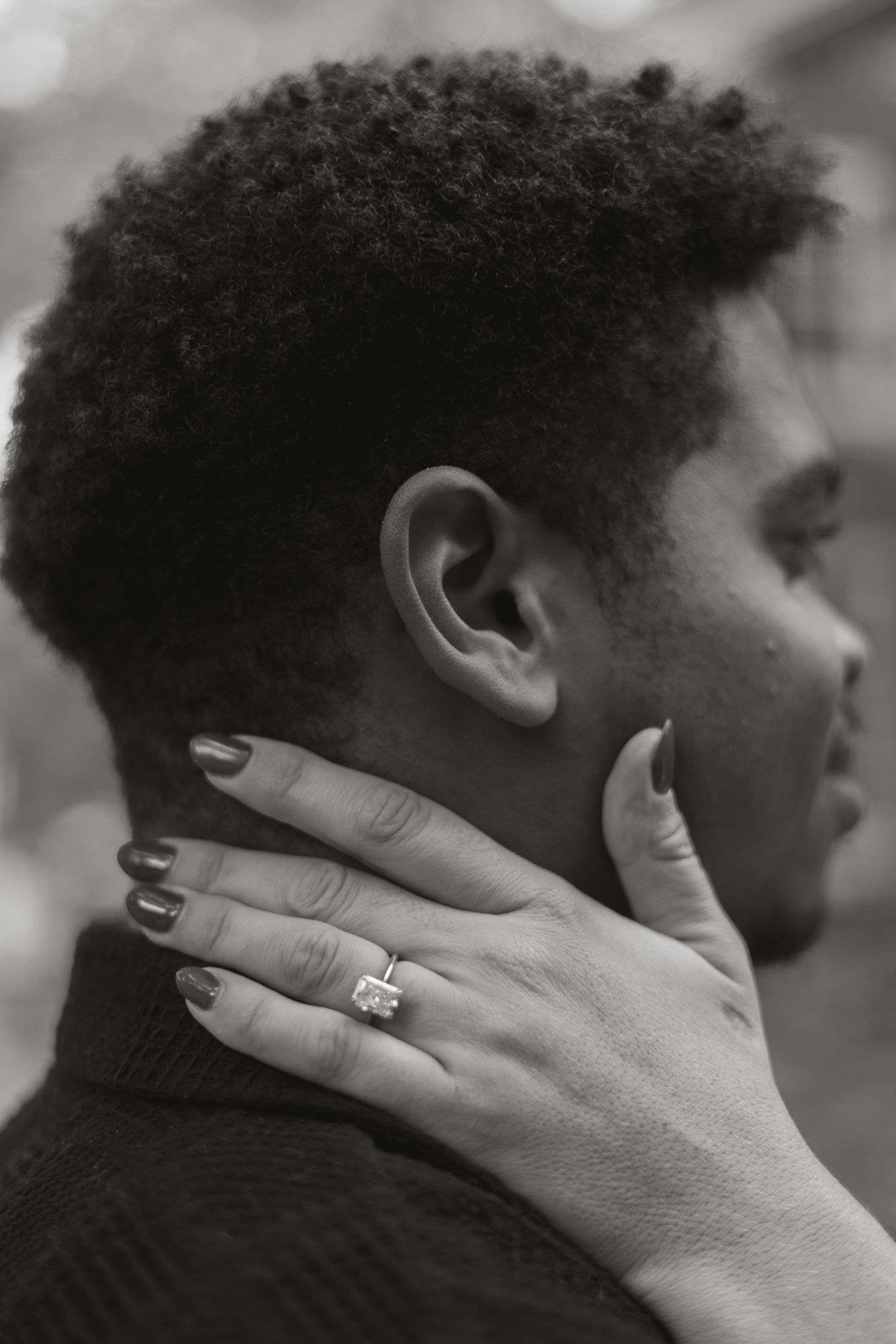 Black and white photo of a woman's hand with a diamond ring resting on a man's neck.