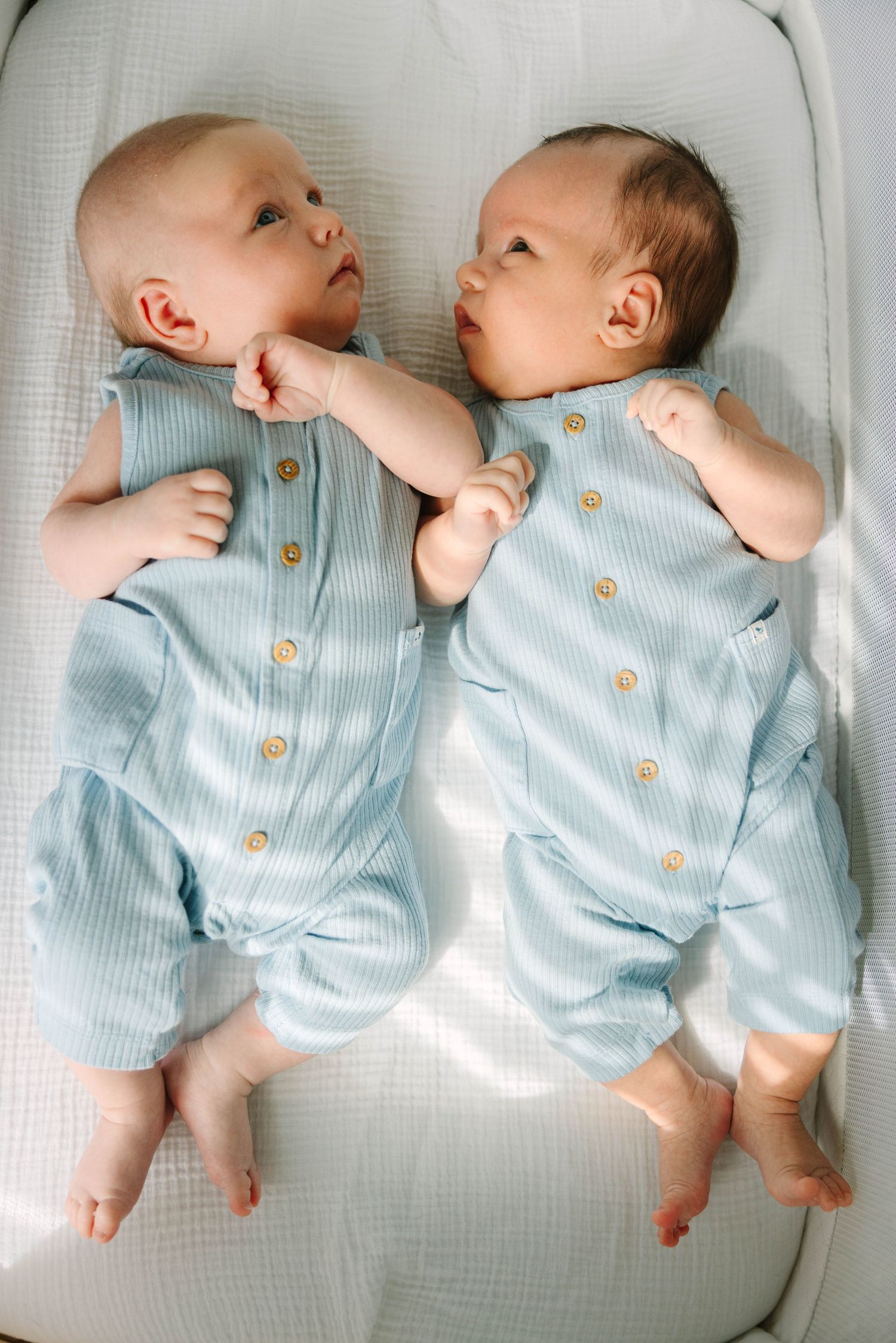Twin newborn babies in matching light blue ribbed rompers lying side by side.