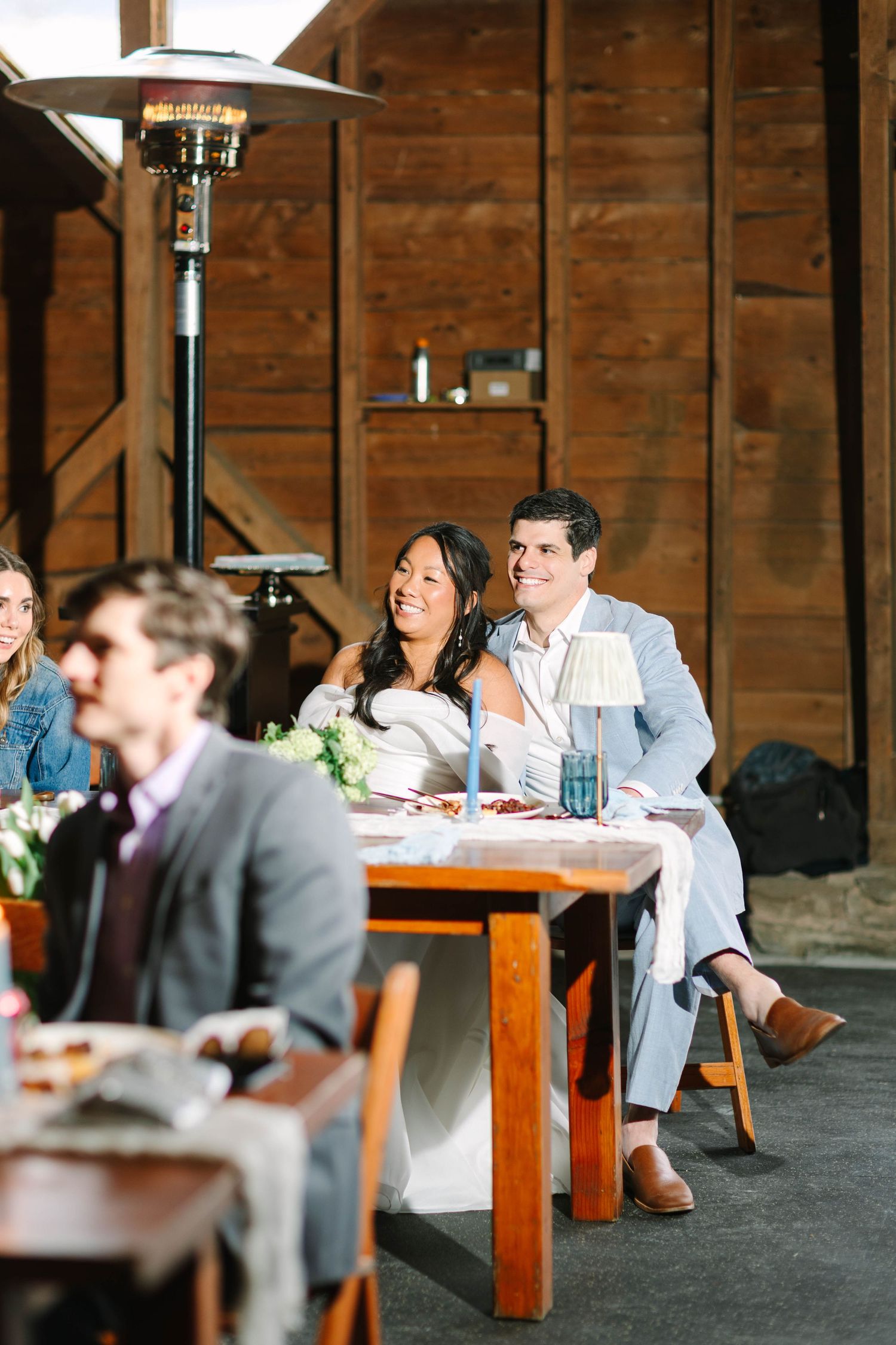 Bride and groom share a joyful moment seated at sweetheart table during barn wedding reception.